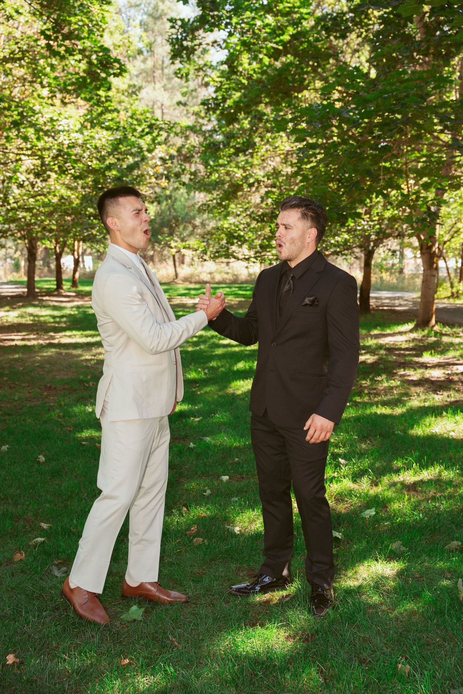 Two people in contrasting outfits playfully interact in a sunny park setting with green grass and trees.