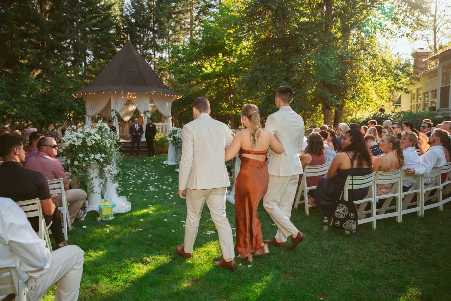 Guests celebrating at an outdoor wedding reception with golden sunlight filtering through trees.