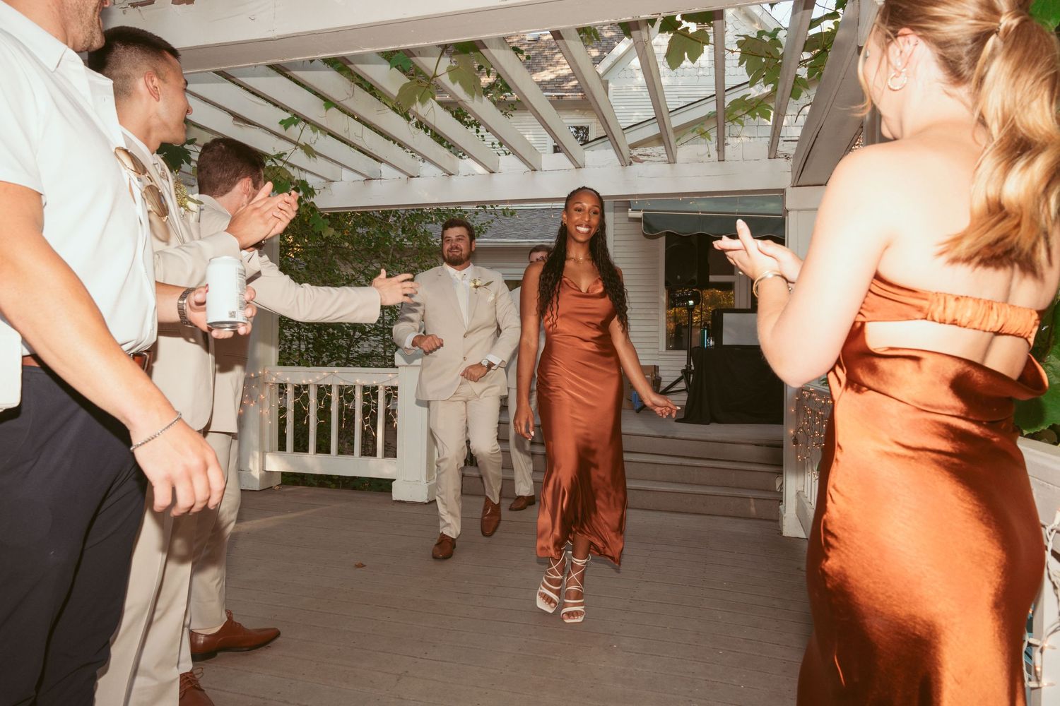 Wedding guests in formal attire dancing and celebrating on an outdoor covered patio.