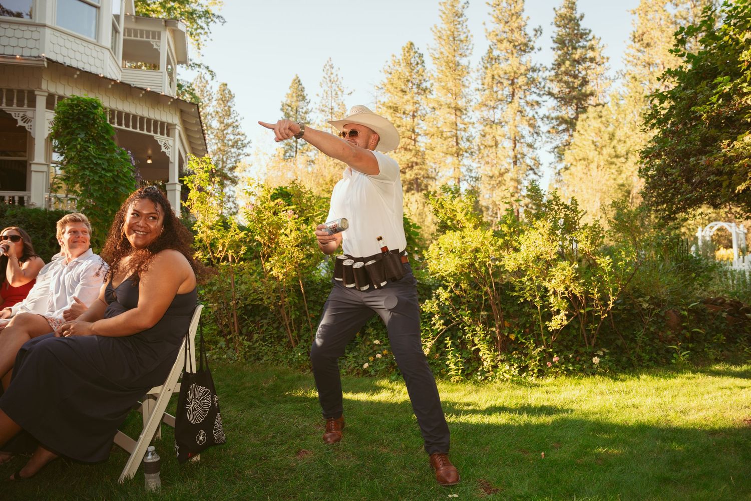 Guest dances energetically at outdoor wedding reception with tall pine trees in background.
