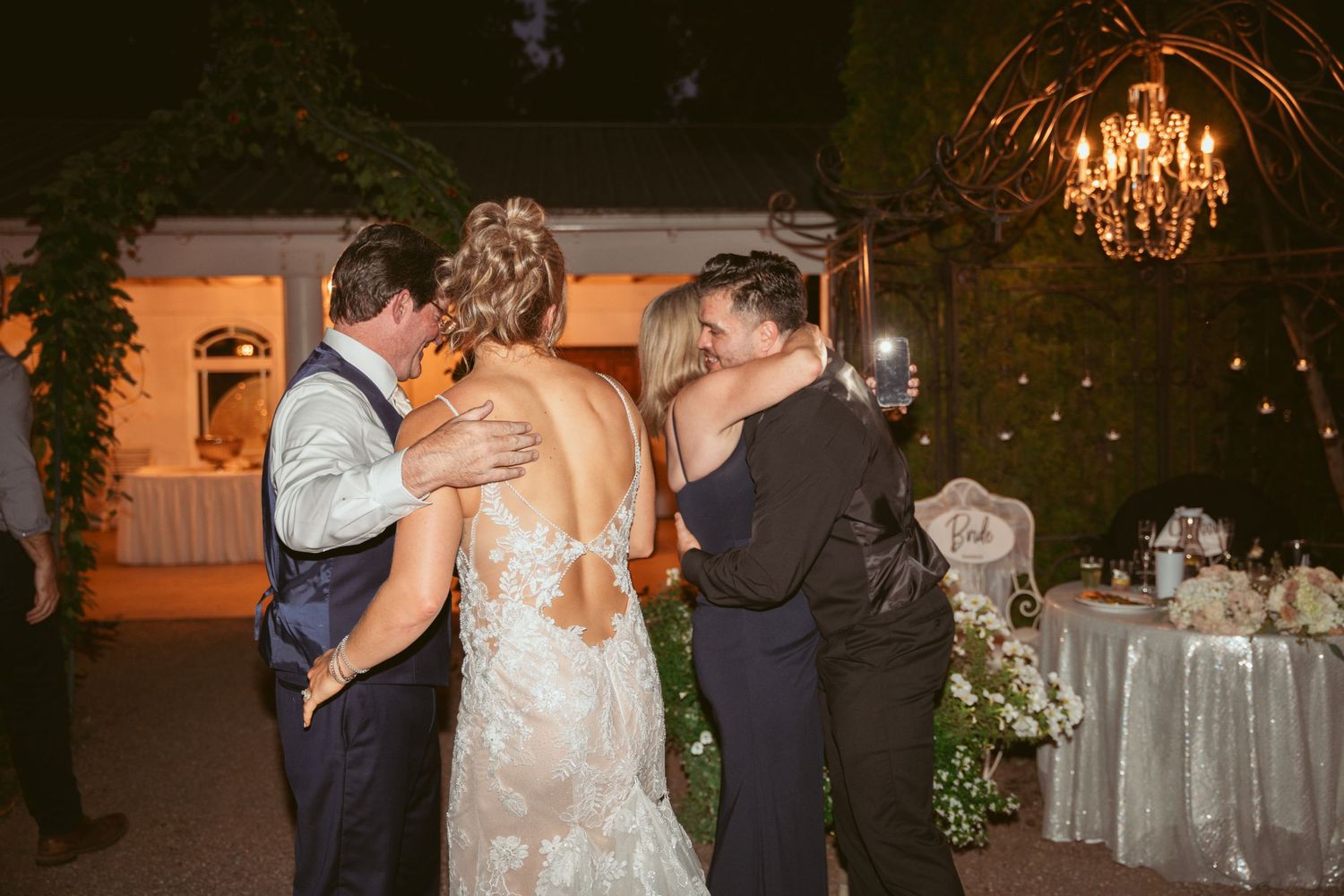 Couples slow dancing together at a romantic outdoor wedding reception with string lights overhead.