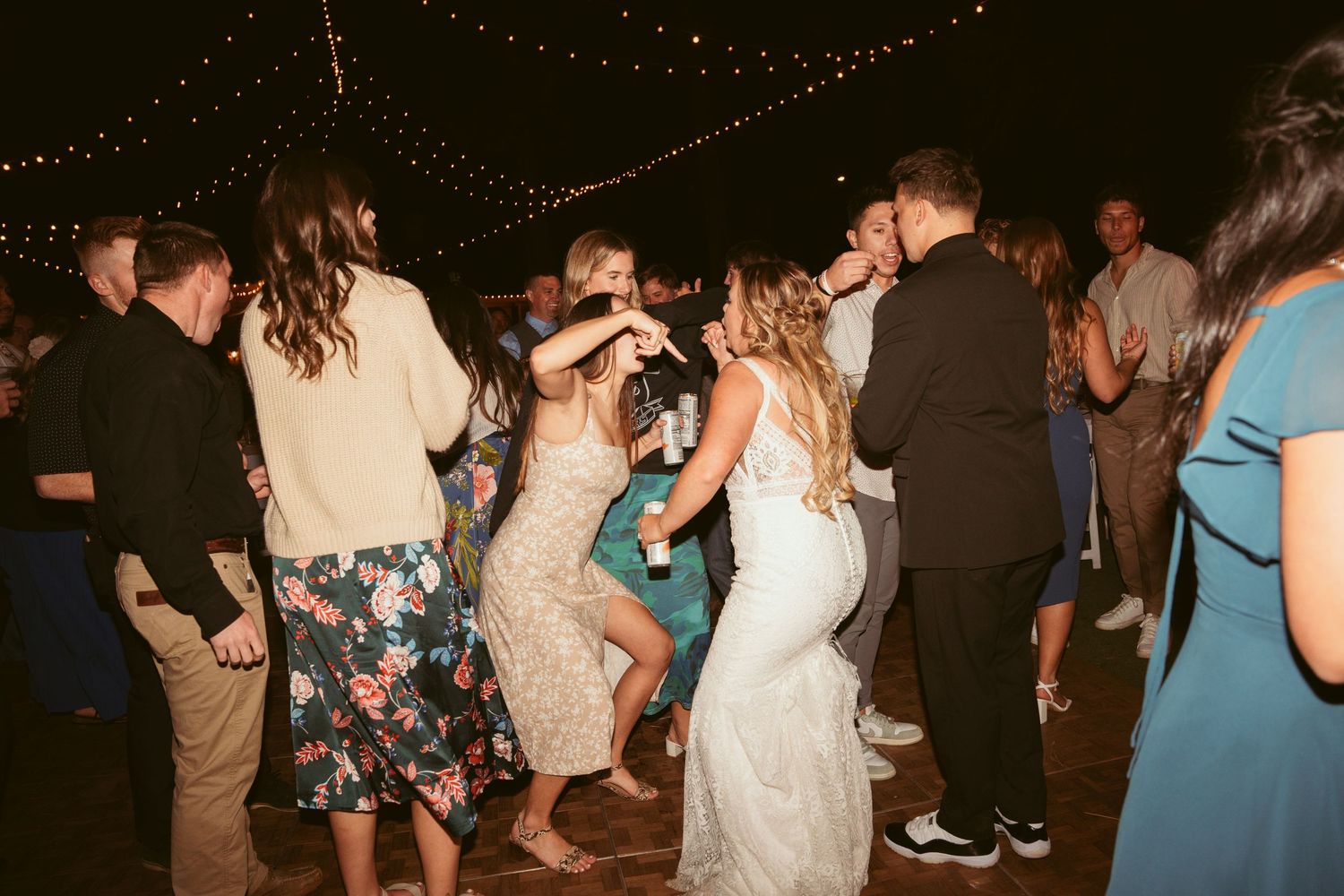 Wedding celebration with guests dancing under string lights at an outdoor venue.