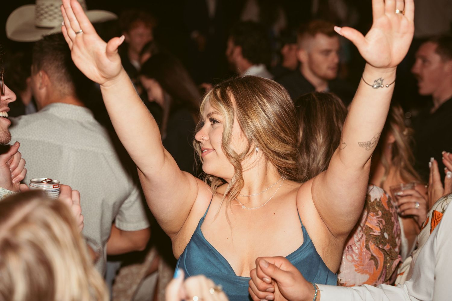 People with raised hands dancing and celebrating at nighttime wedding reception.
