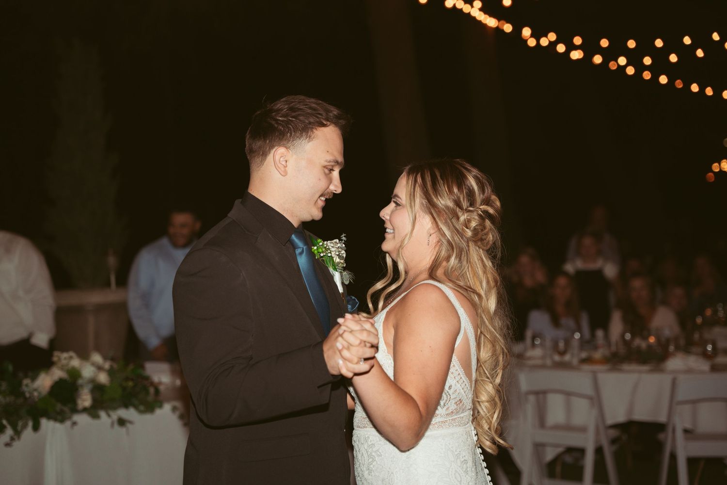Romantic first dance at an outdoor evening wedding reception under twinkling lights.