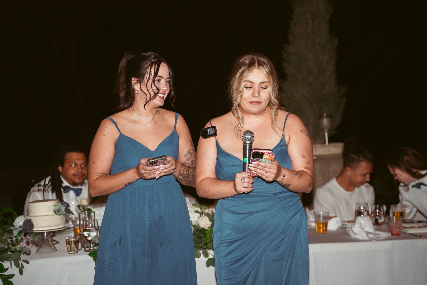 Wedding guests in blue dresses socialize at an outdoor evening reception.