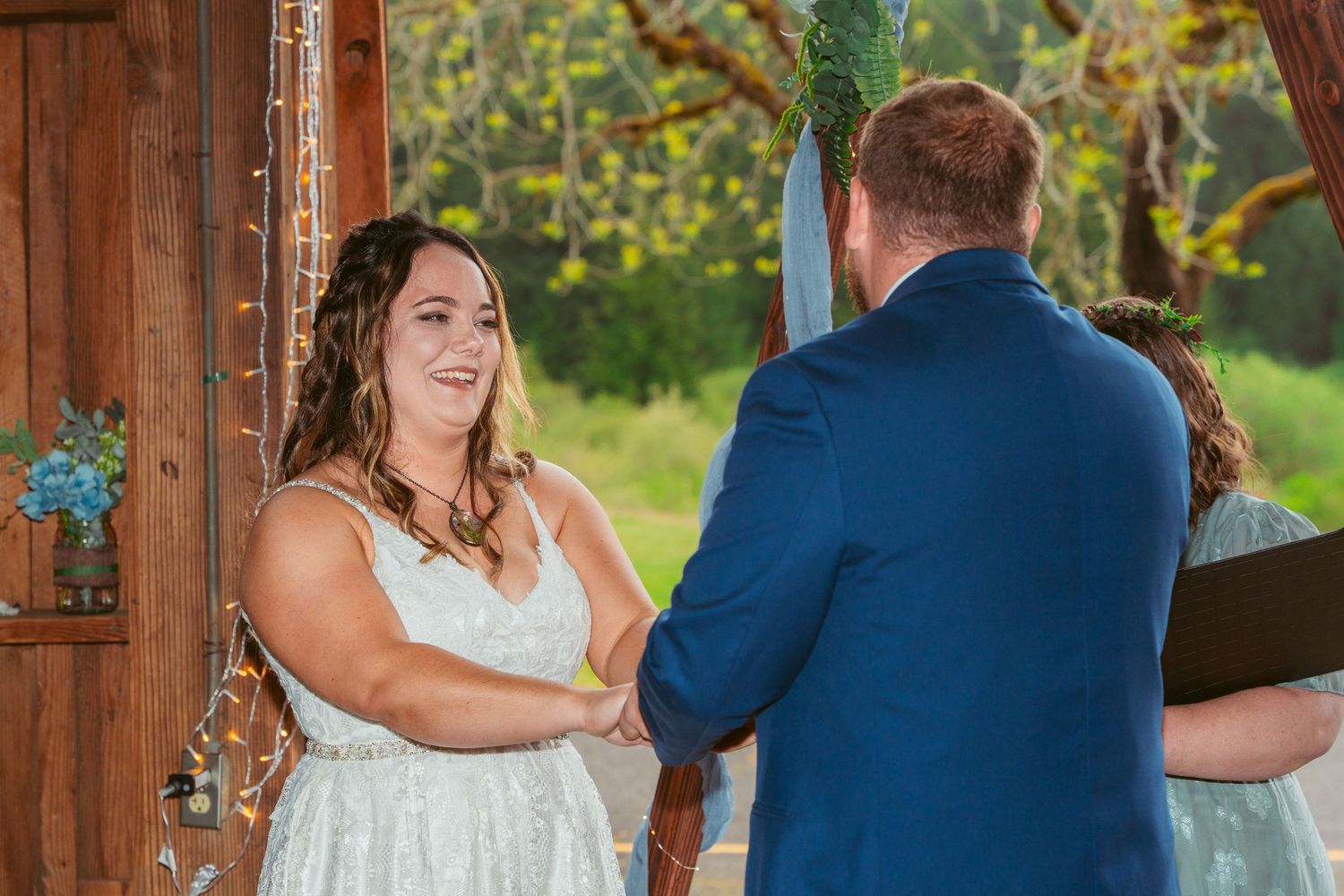 Intimate wedding ceremony in wooden barn decorated with twinkle lights and greenery.