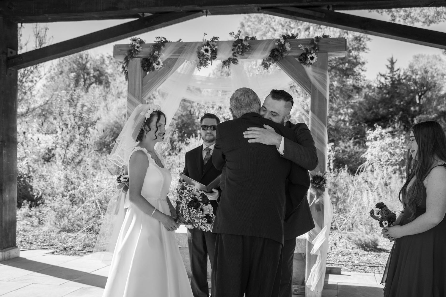 Black and white panorama of wedding ceremony proceedings under covered pavilion.