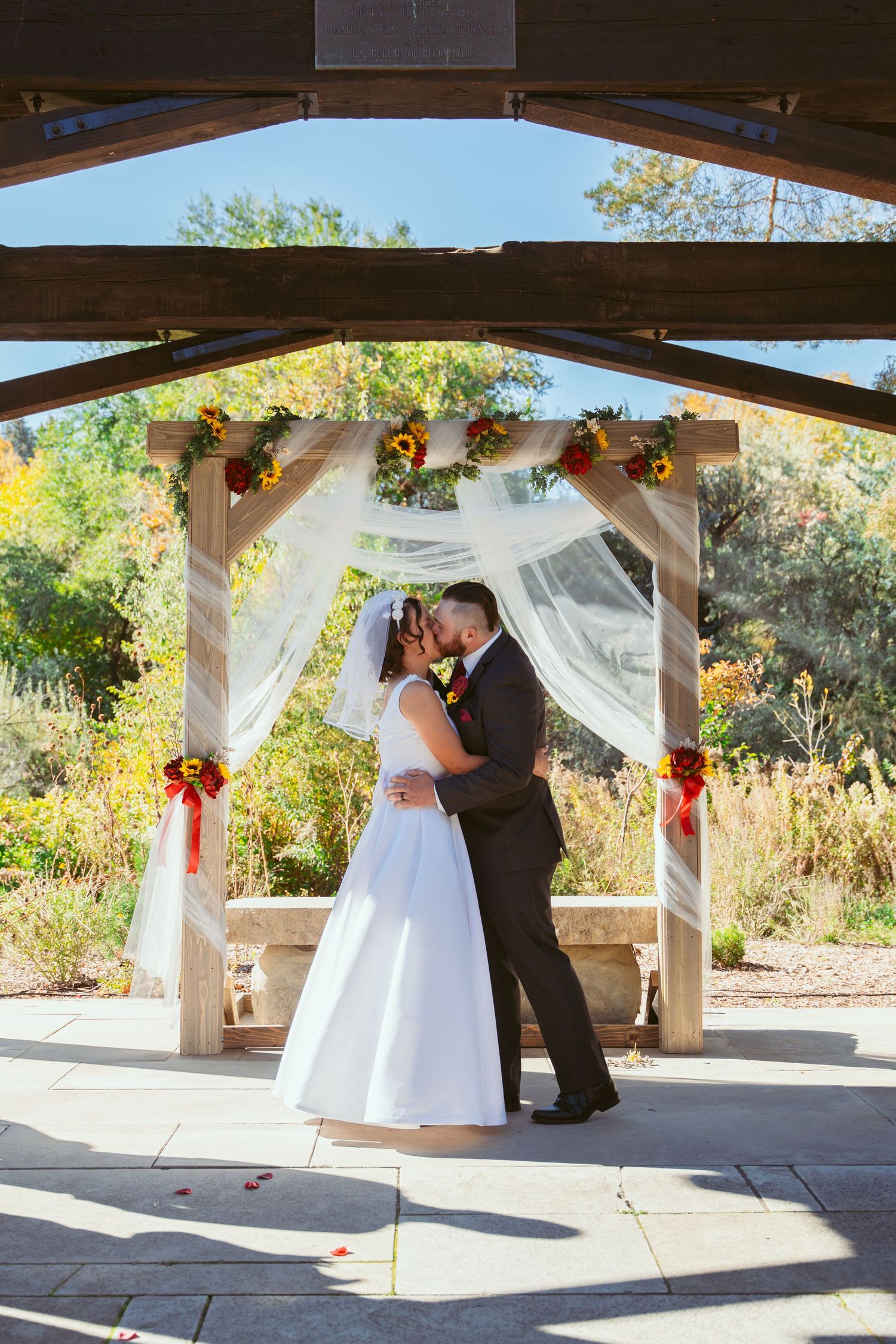 Wedding ceremony in progress under a rustic wooden pavilion with flowing white drapes.