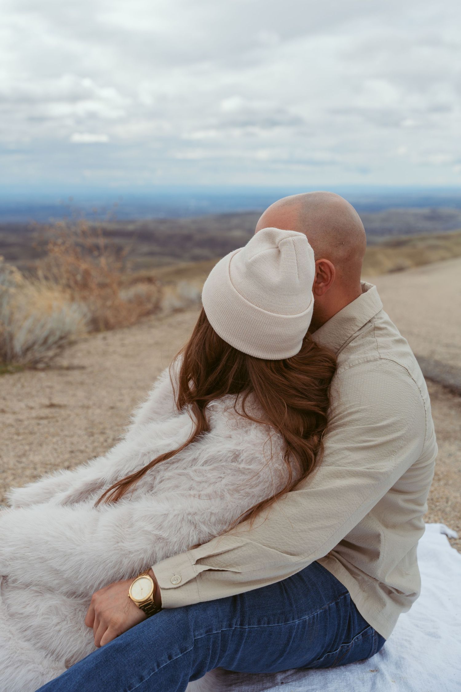 Couple sharing intimate moment while resting on white blanket in desert landscape.