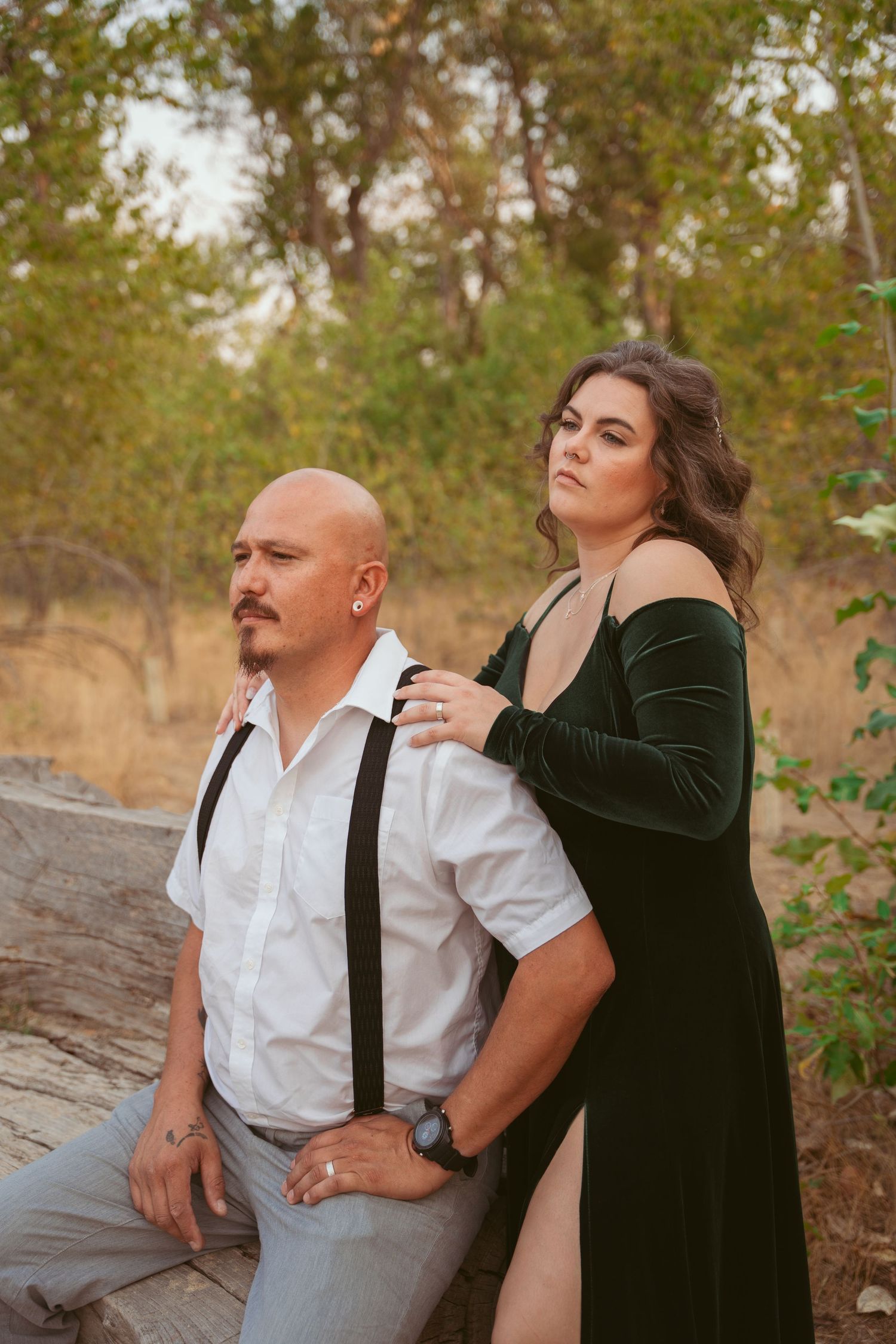A romantic couple embraces while standing together in a natural outdoor setting at sunset.