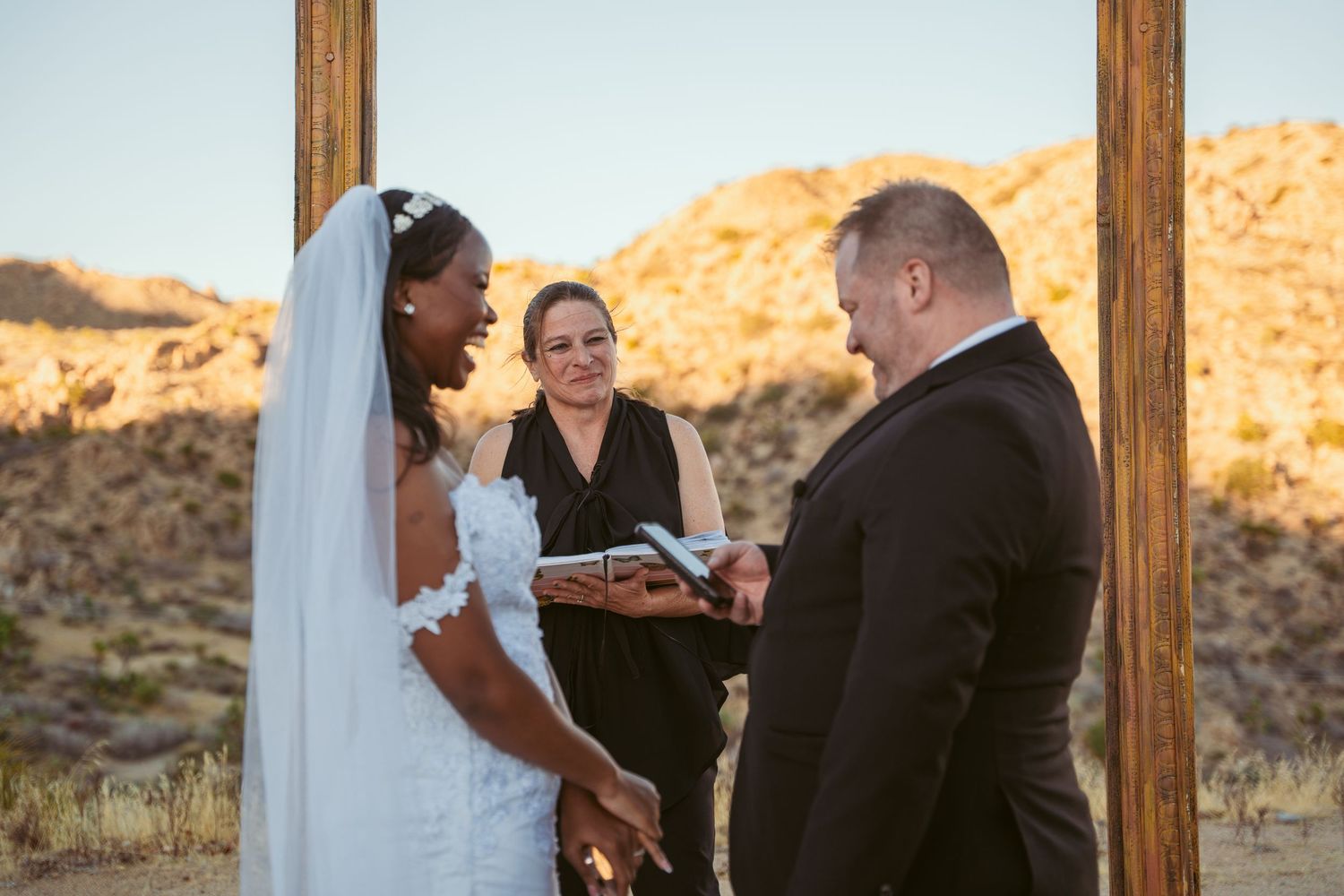 Wedding ceremony with officiant and couple exchanging vows against golden desert hills.