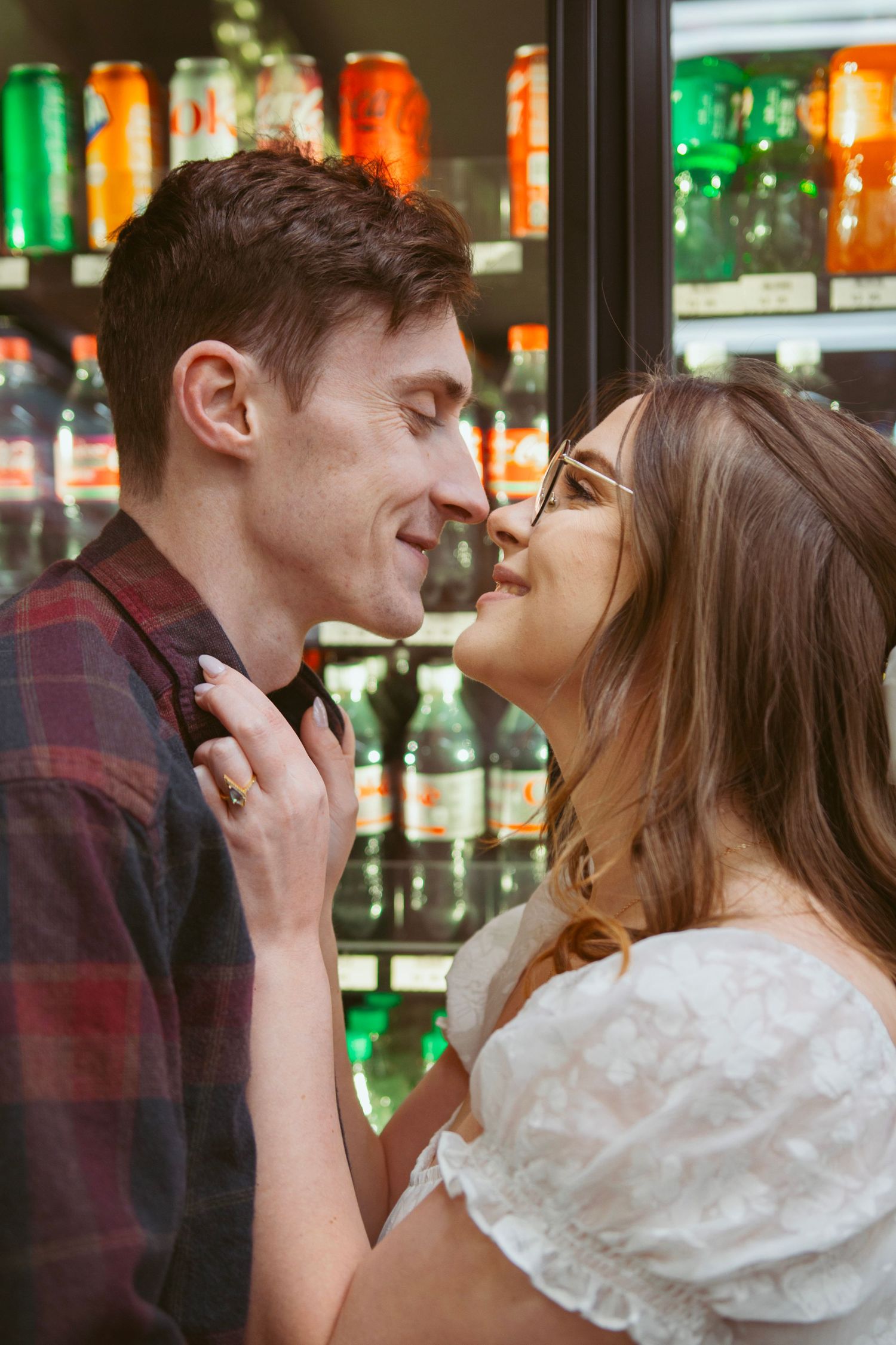 Romantic moment captured between couple in front of illuminated drink coolers.