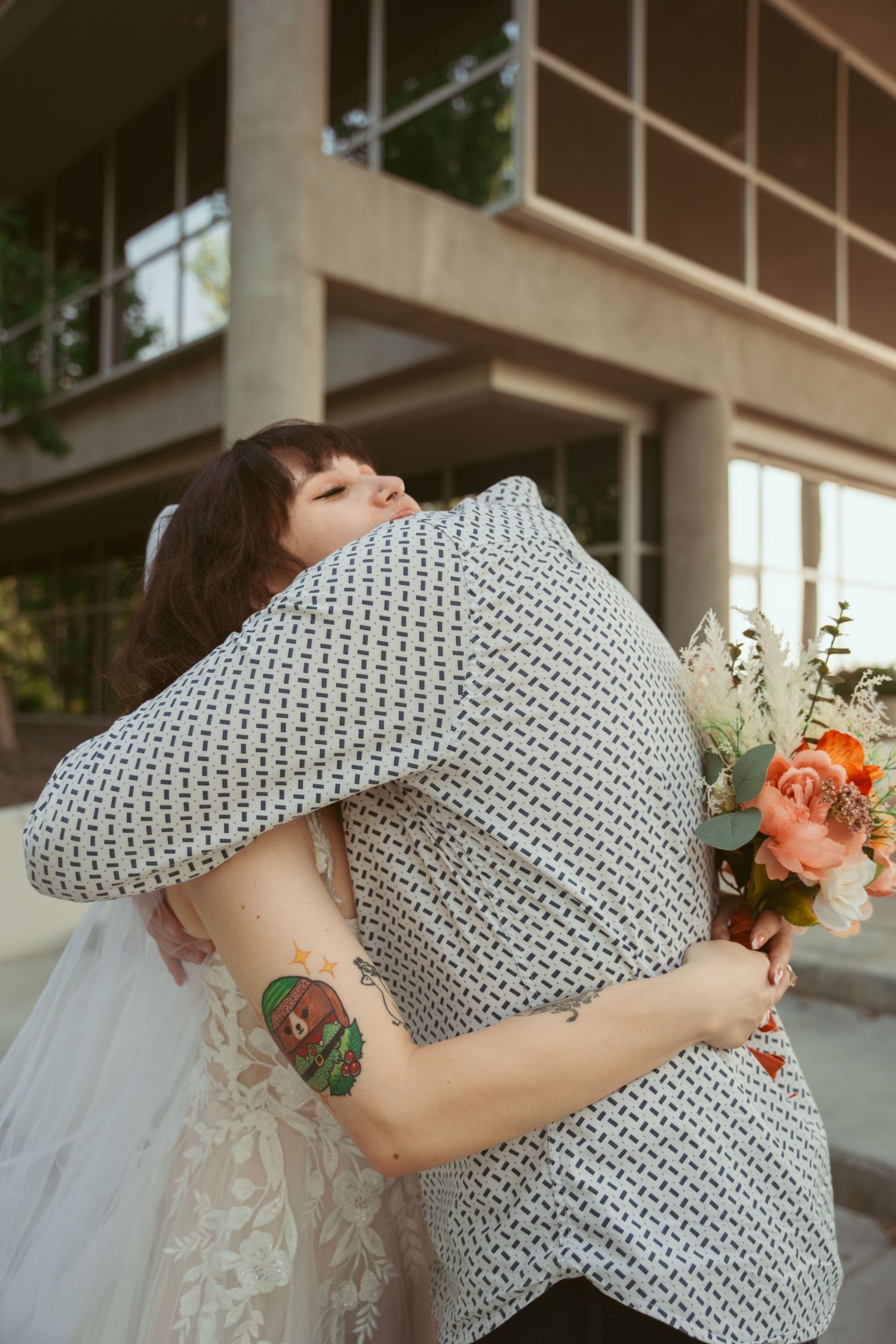 Close-up of emotional embrace showing detailed knit sweater and floral bouquet.