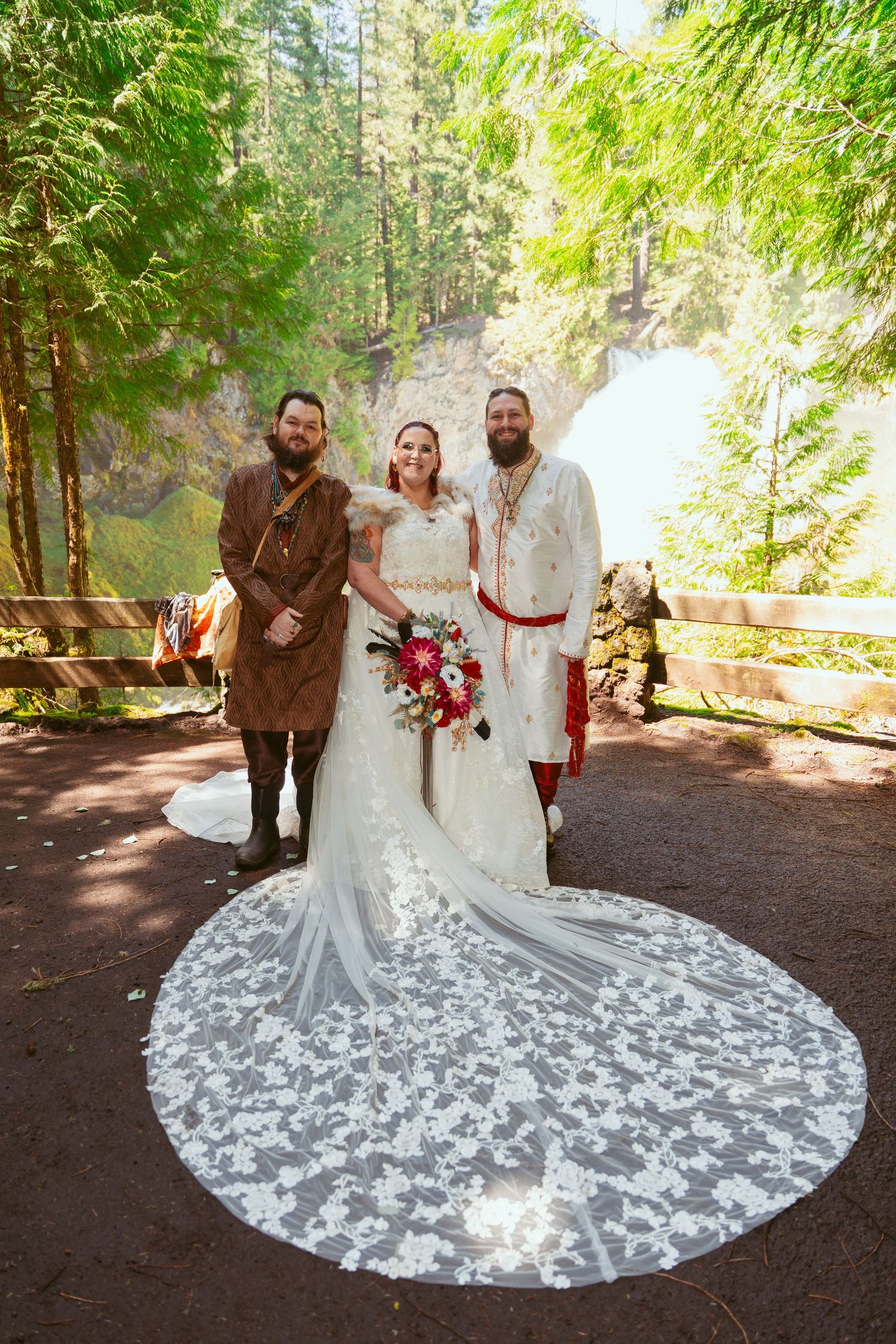 Beautiful lace train of a white wedding dress spreads across forest ground during outdoor ceremony.