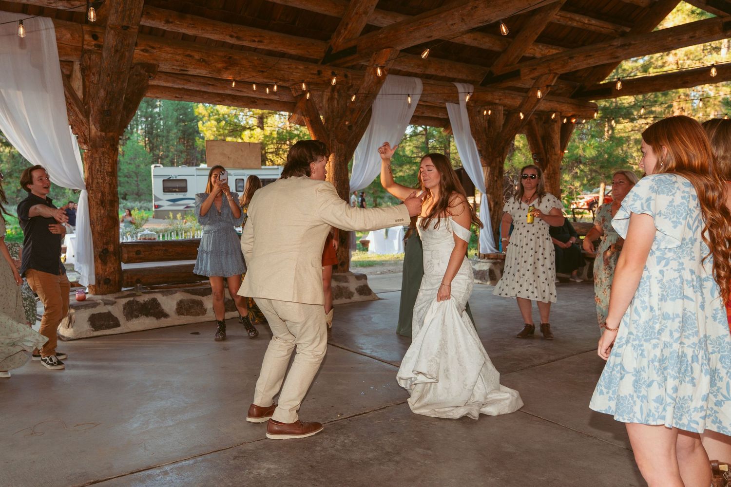 Couples dancing at an outdoor wedding reception under a covered wooden structure.