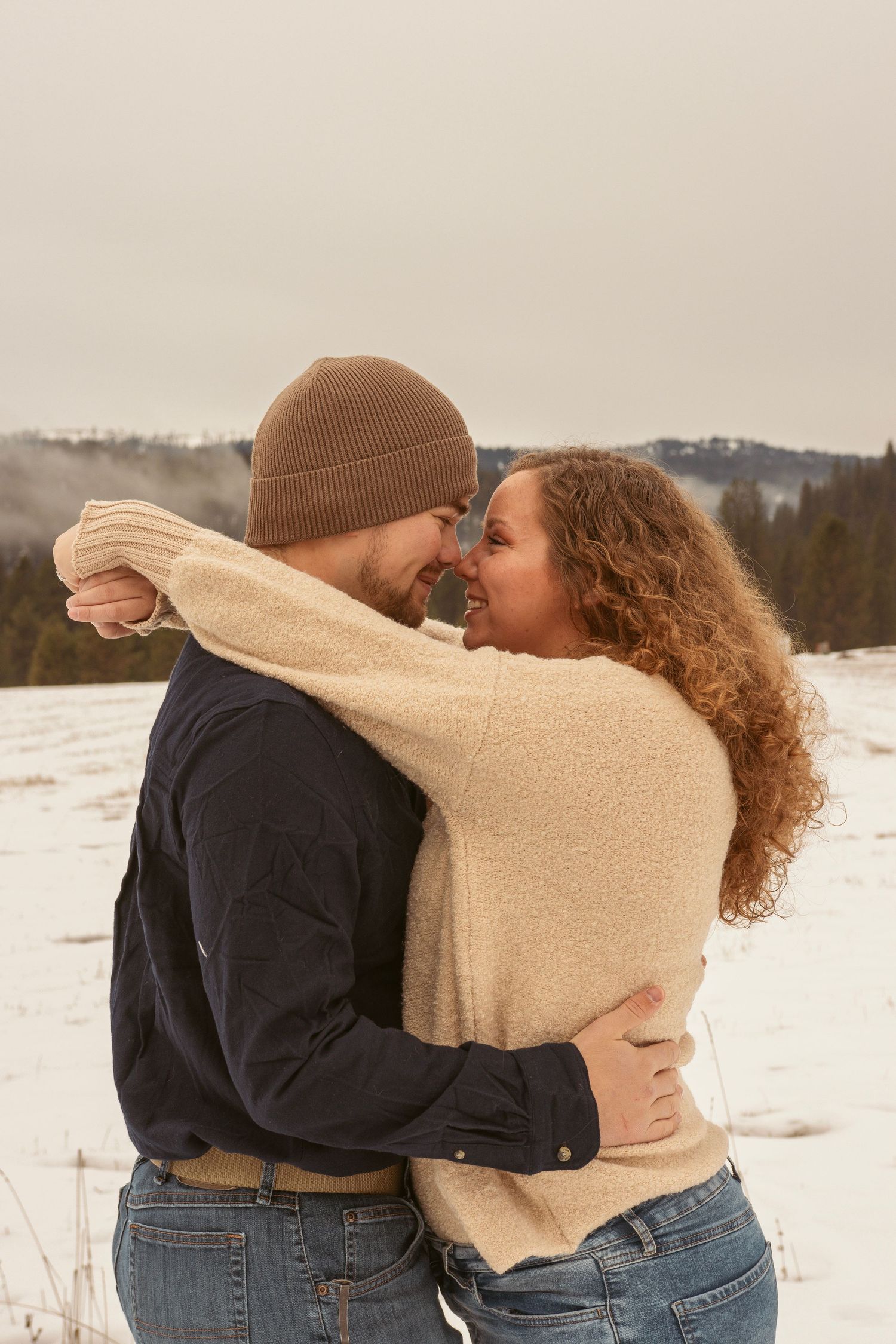 Romantic embrace in cream sweater and dark jacket against snowy winter backdrop.