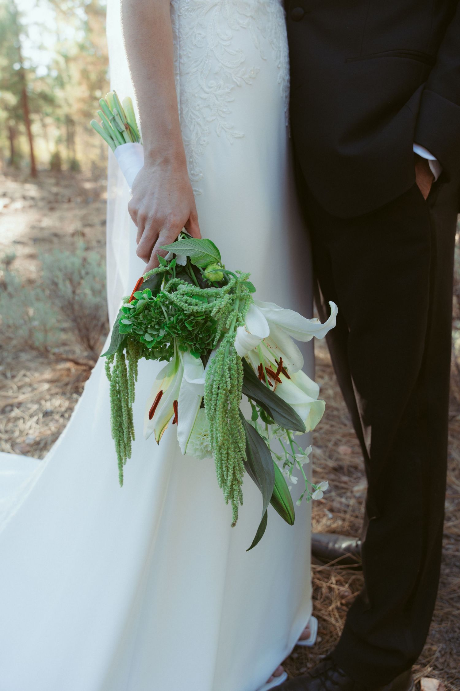 Close-up of a bridal bouquet featuring white flowers and cascading greenery against a wedding dress.