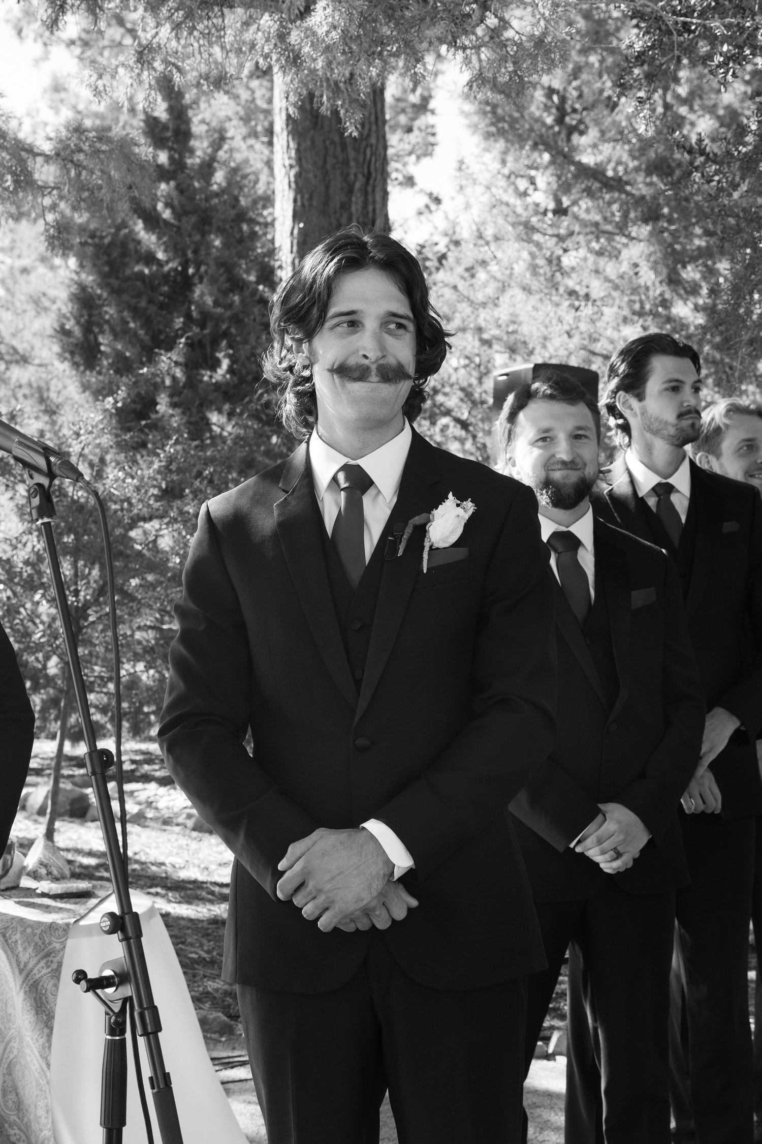 Black and white photo of groomsmen standing in formation at an outdoor wedding ceremony.
