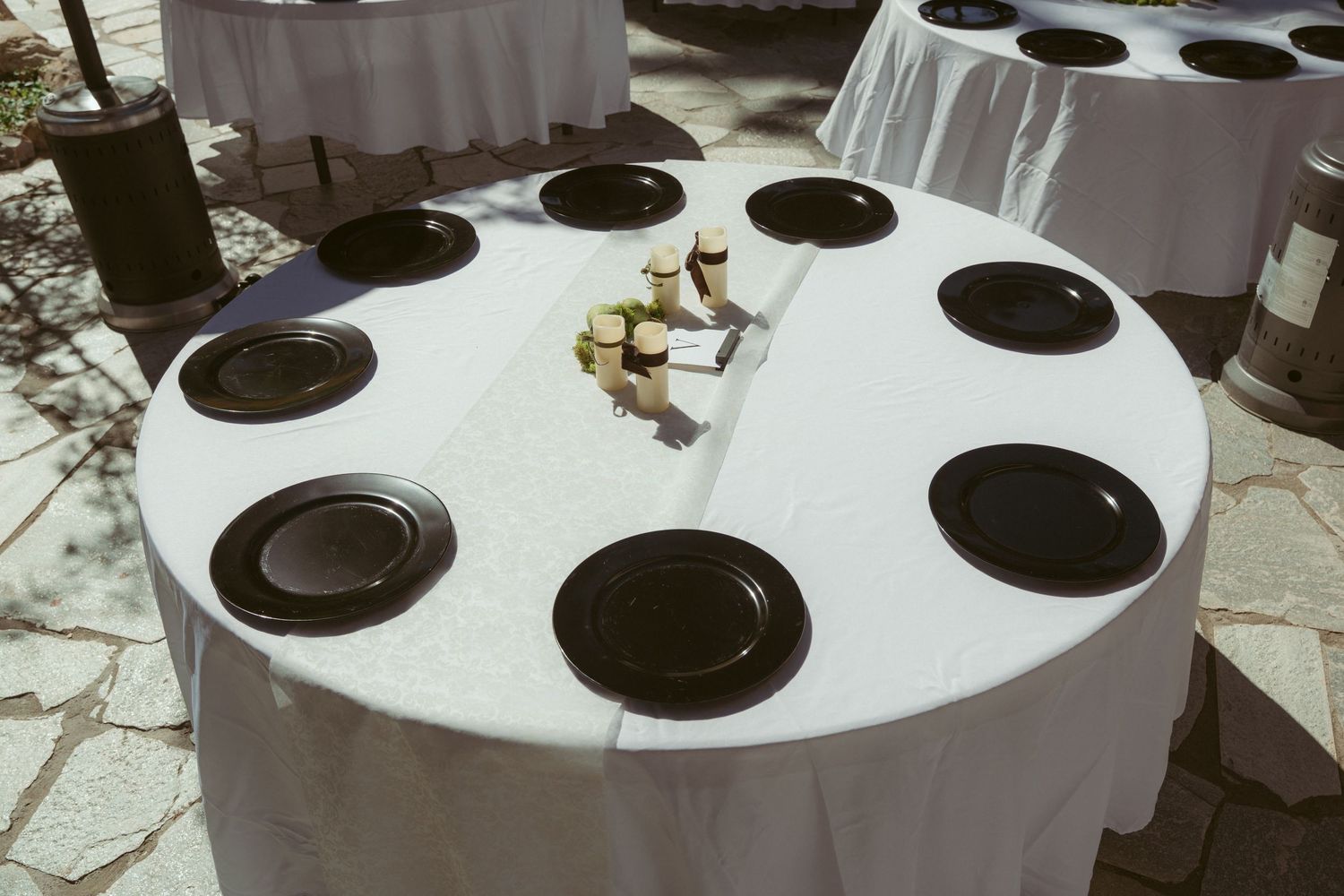 Round reception tables with white tablecloths and black charger plates set for a wedding.