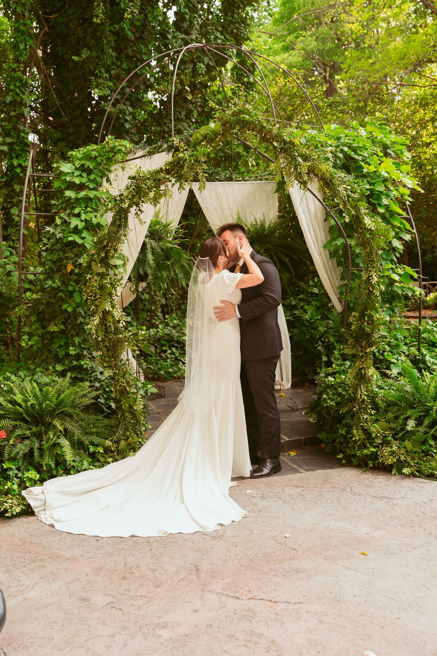 Newlyweds share their first kiss under an ivy-covered wedding arch.