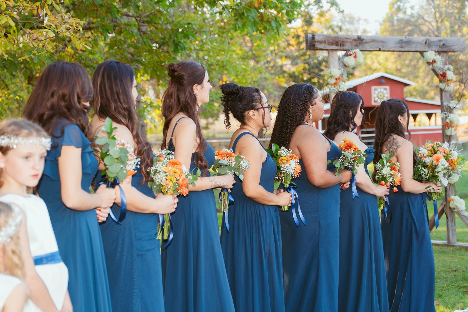 Row of bridesmaids in navy blue dresses standing together at outdoor autumn wedding.