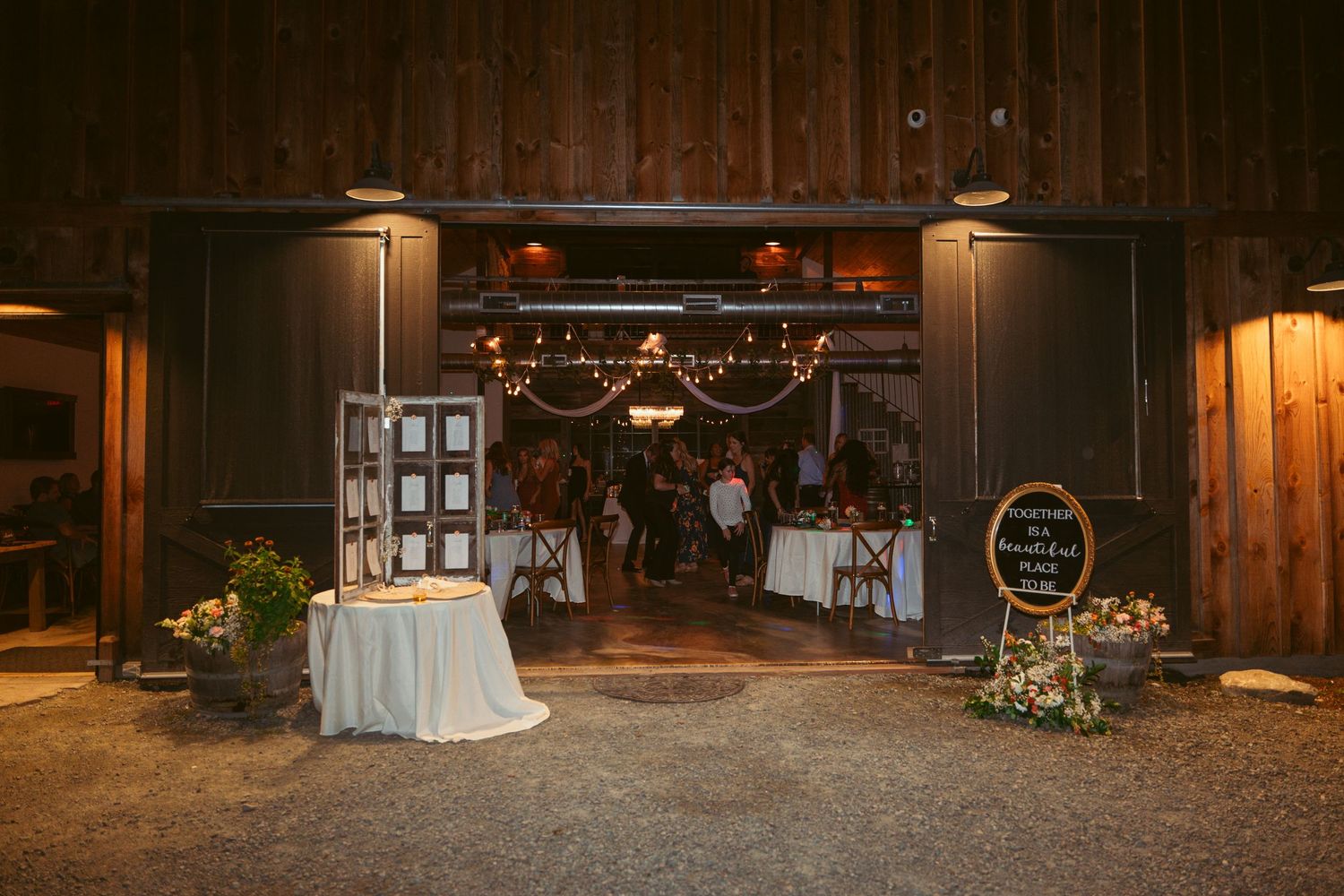 Rustic barn wedding venue entrance decorated with string lights and white table settings at dusk.