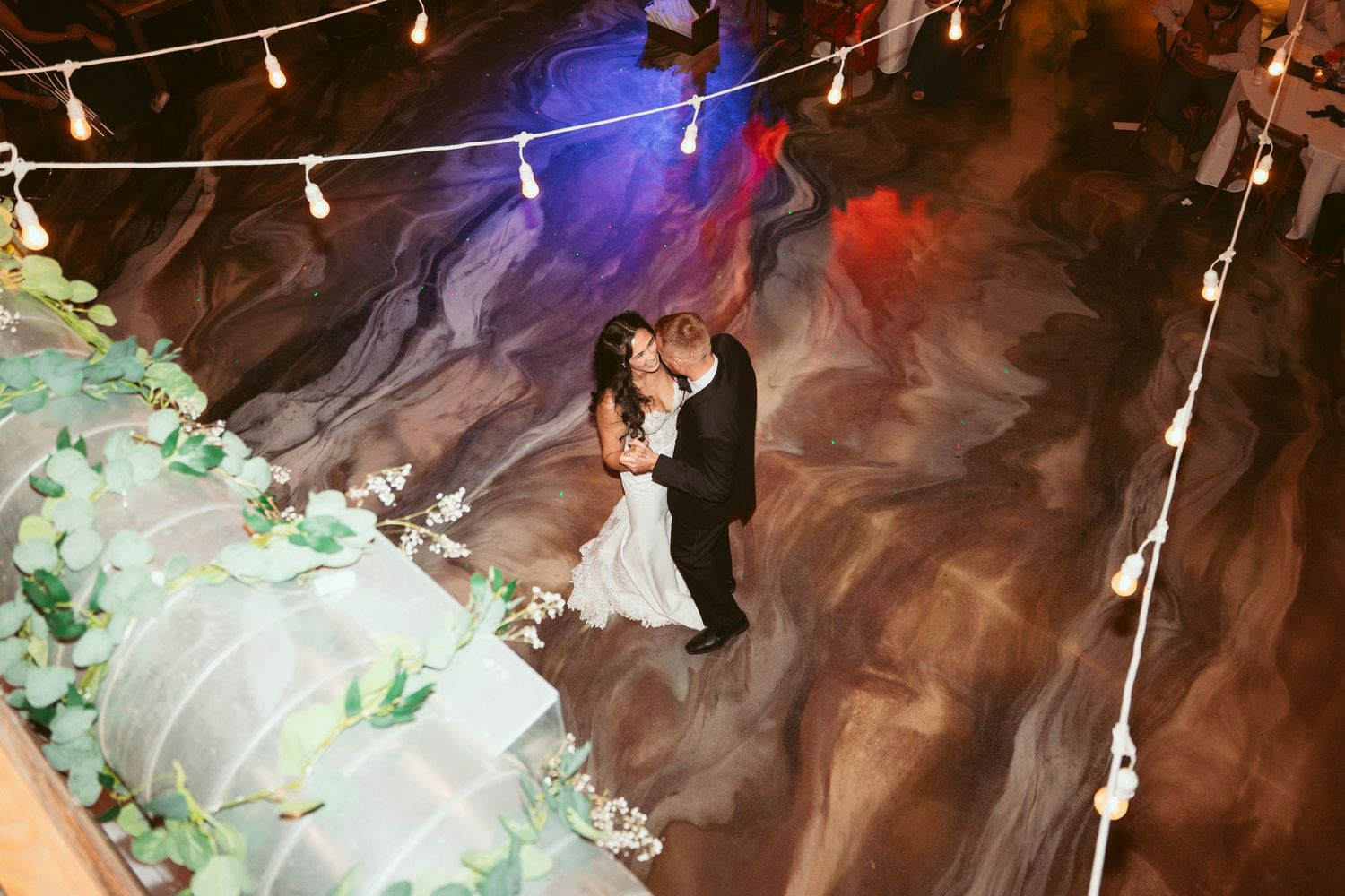 Wedding reception dance floor illuminated with colorful lights and string lighting overhead.