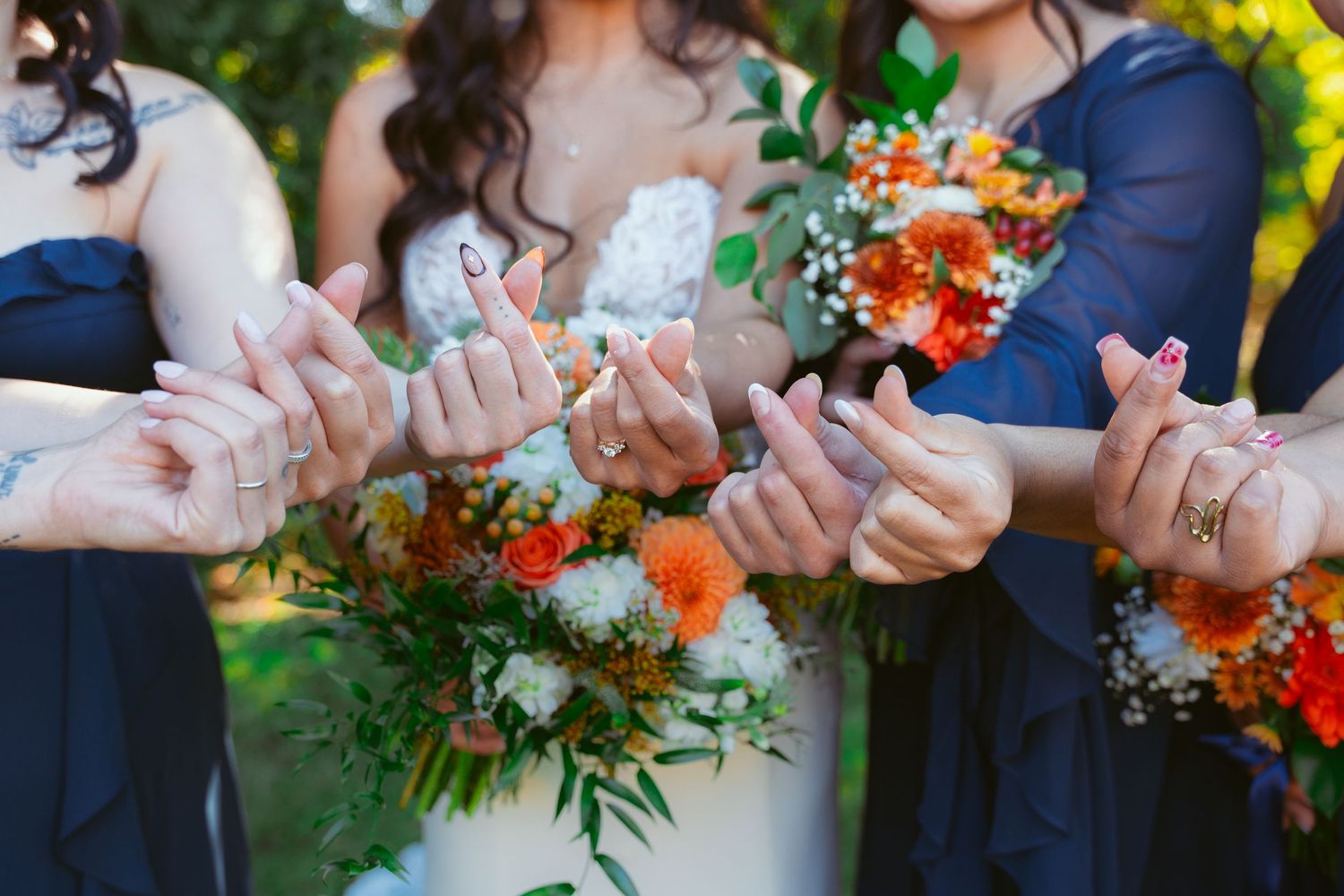 Wedding party members hold hands in a line showing off navy dresses and colorful floral bouquets.