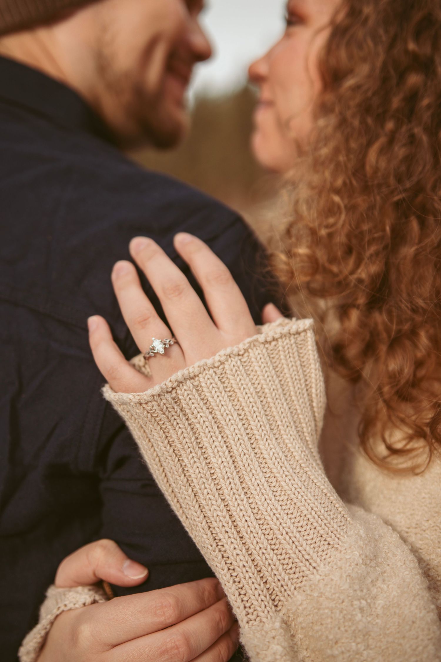 Close-up of couple's hands with engagement ring and knit sweater details.