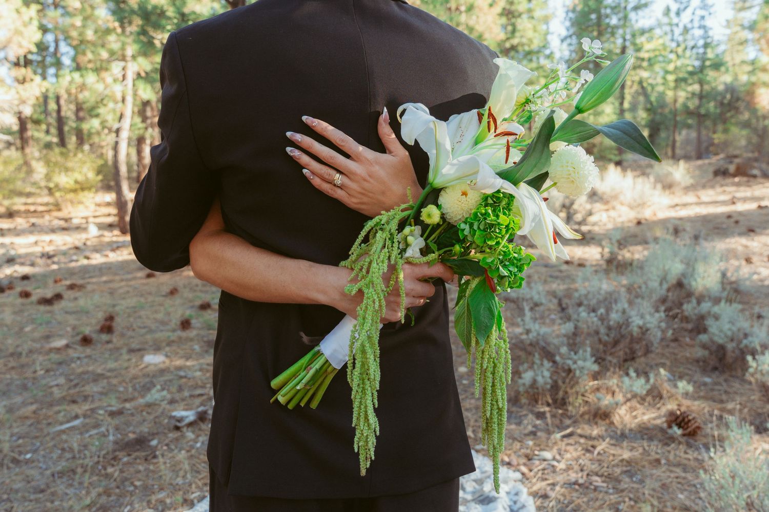 A wedding bouquet with white flowers and greenery held during an outdoor forest ceremony.