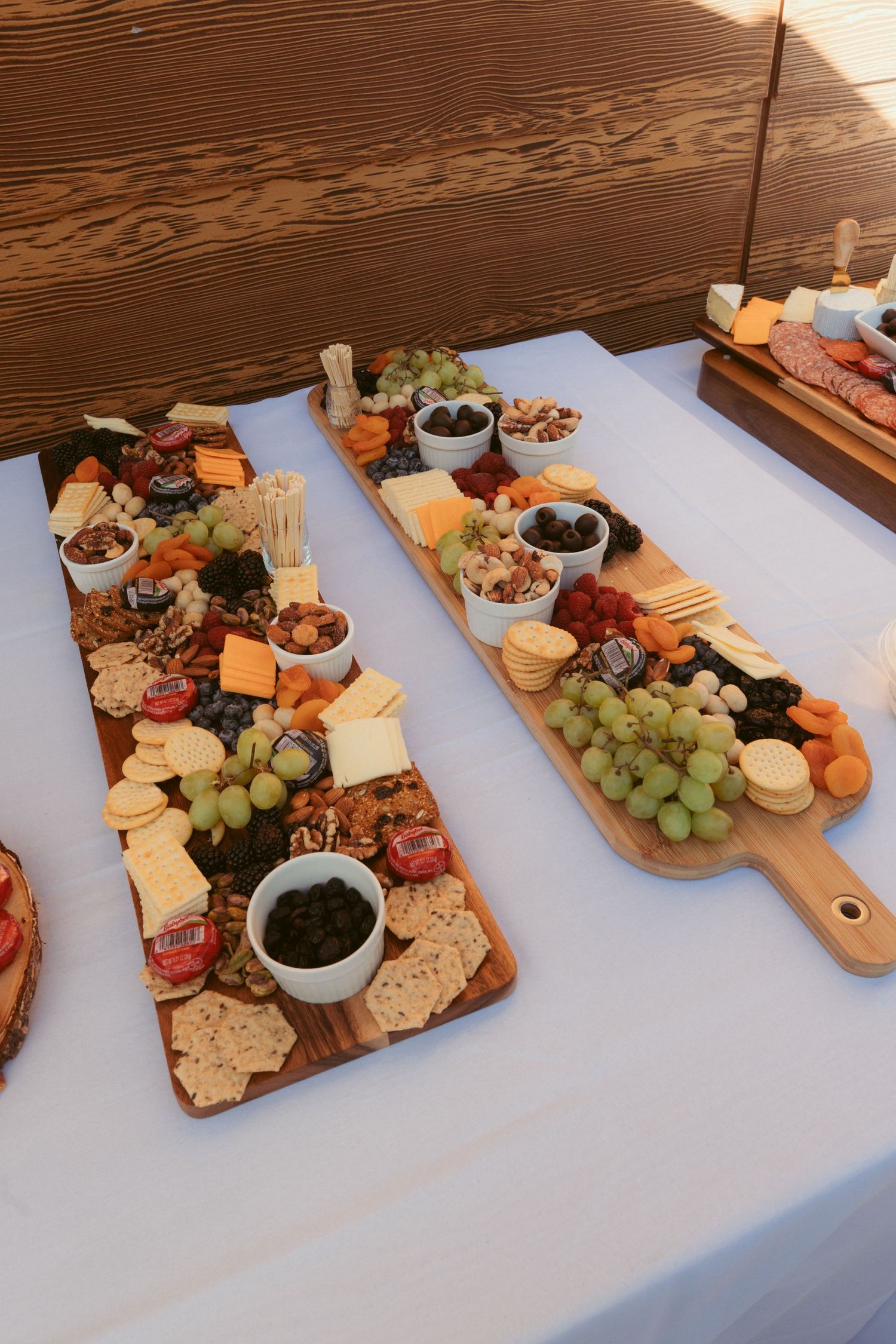Wooden charcuterie boards loaded with cheese, meats, fruits and crackers on white tablecloth.