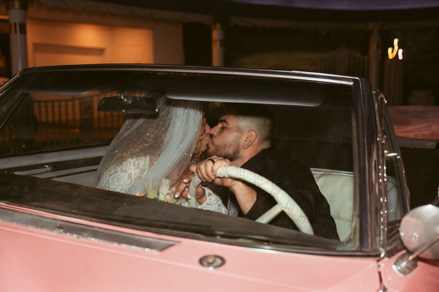 Newlyweds share intimate moments inside a classic pink car after their wedding ceremony.