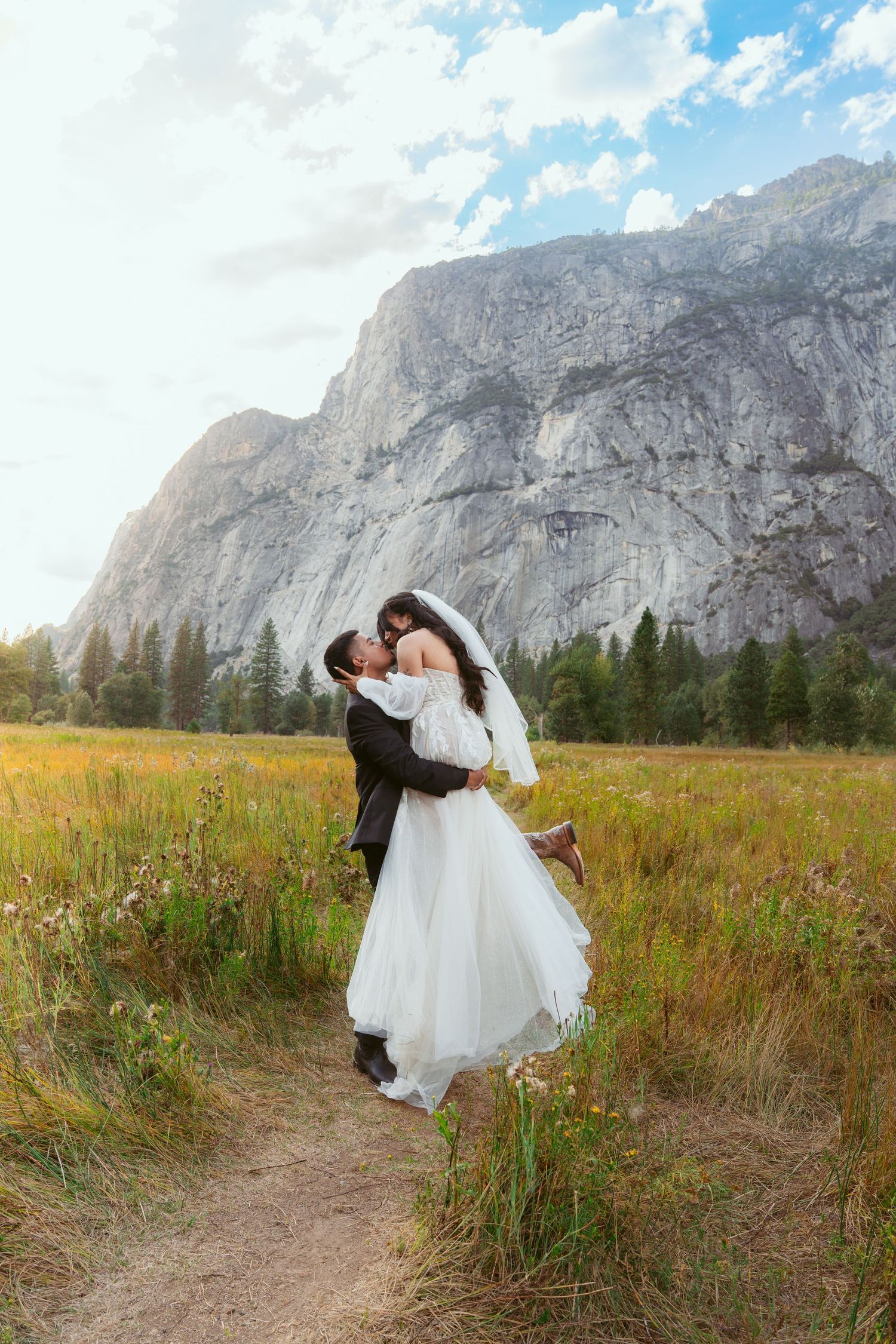 A romantic wedding photo in Yosemite Valley with towering granite cliffs and golden meadow in the background.