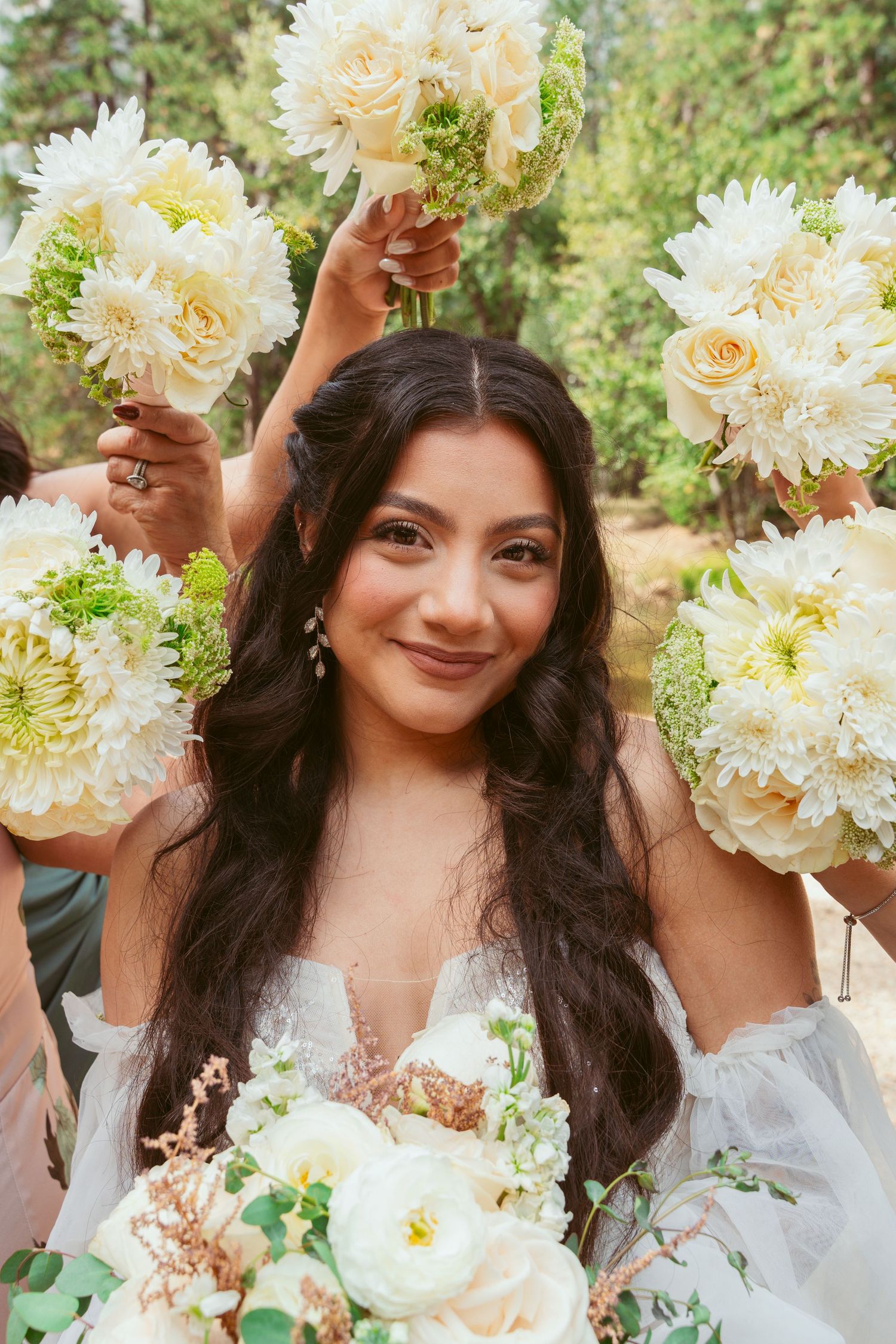 Bride smiling with elegant white floral bouquet against natural greenery background.