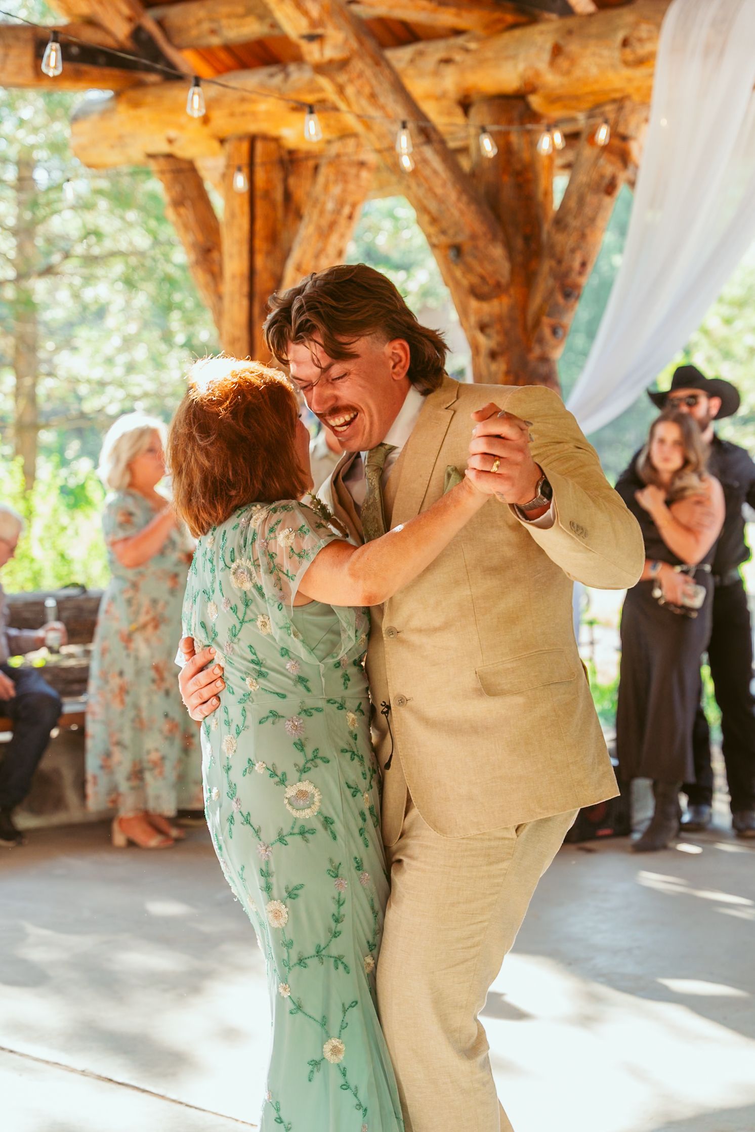 Dancing couple in khaki and mint green twirling beneath rustic wooden beams.