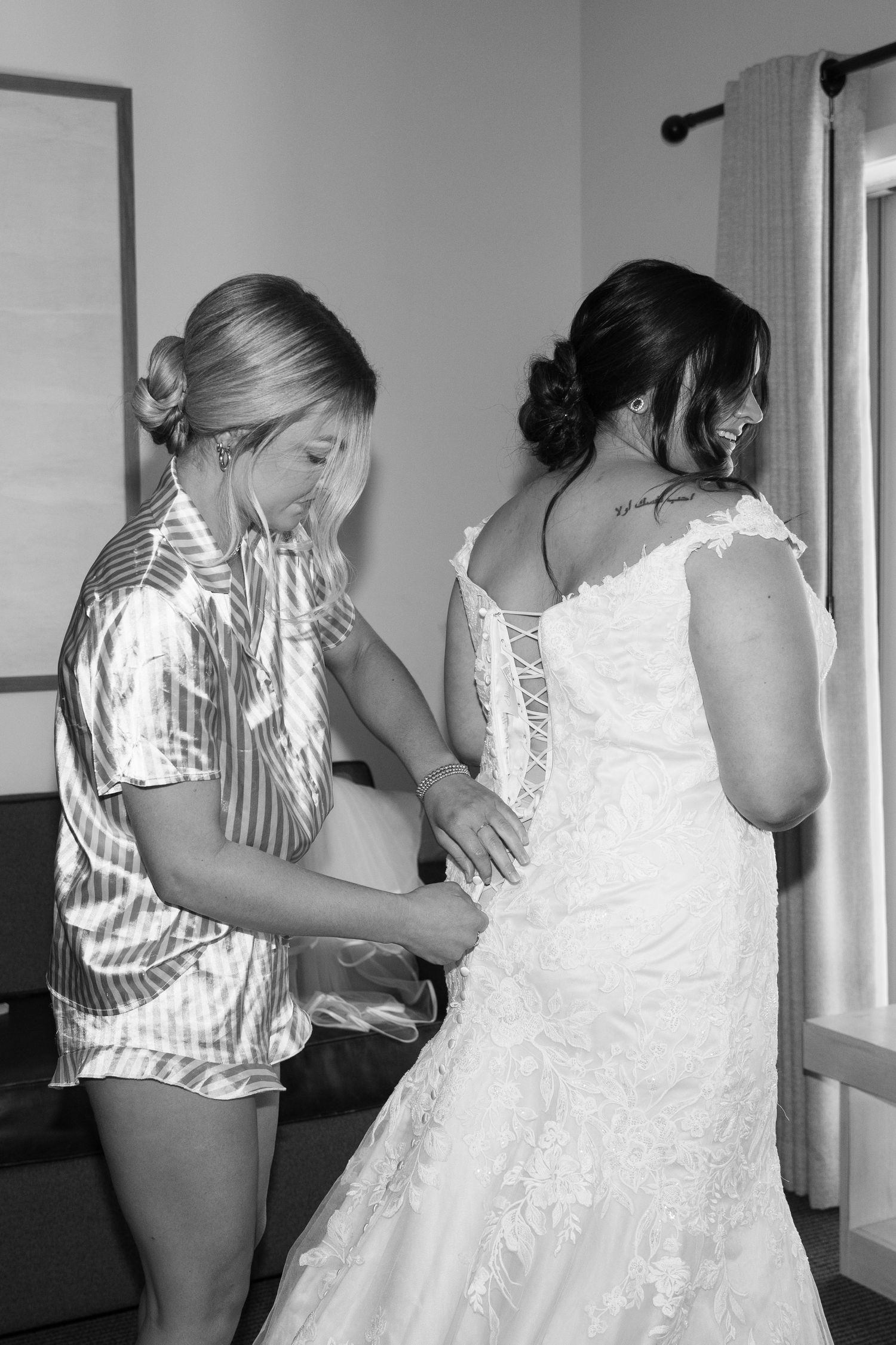 Black and white photo showing final adjustments being made to a detailed lace wedding gown.