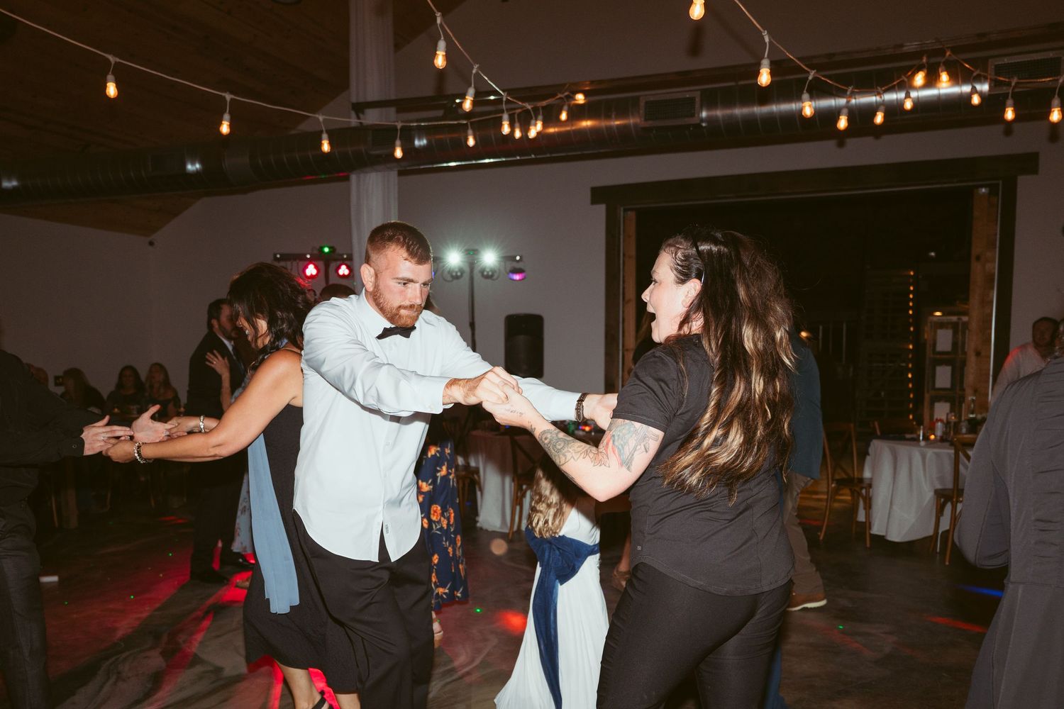 Party guests dancing in pairs under ambient string lights at an indoor venue.