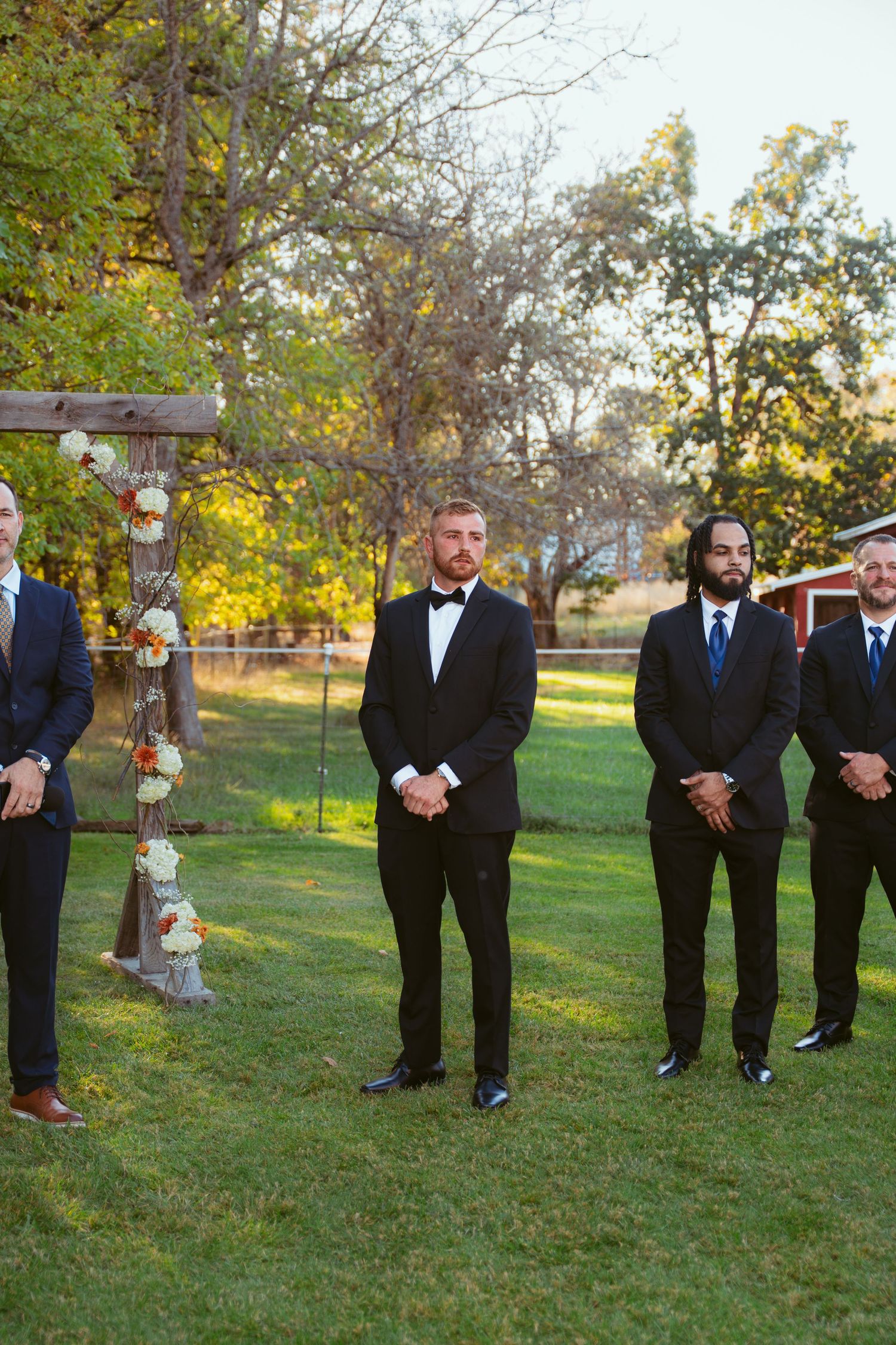 Groomsmen lined up outdoors on grass with autumn trees in the background.