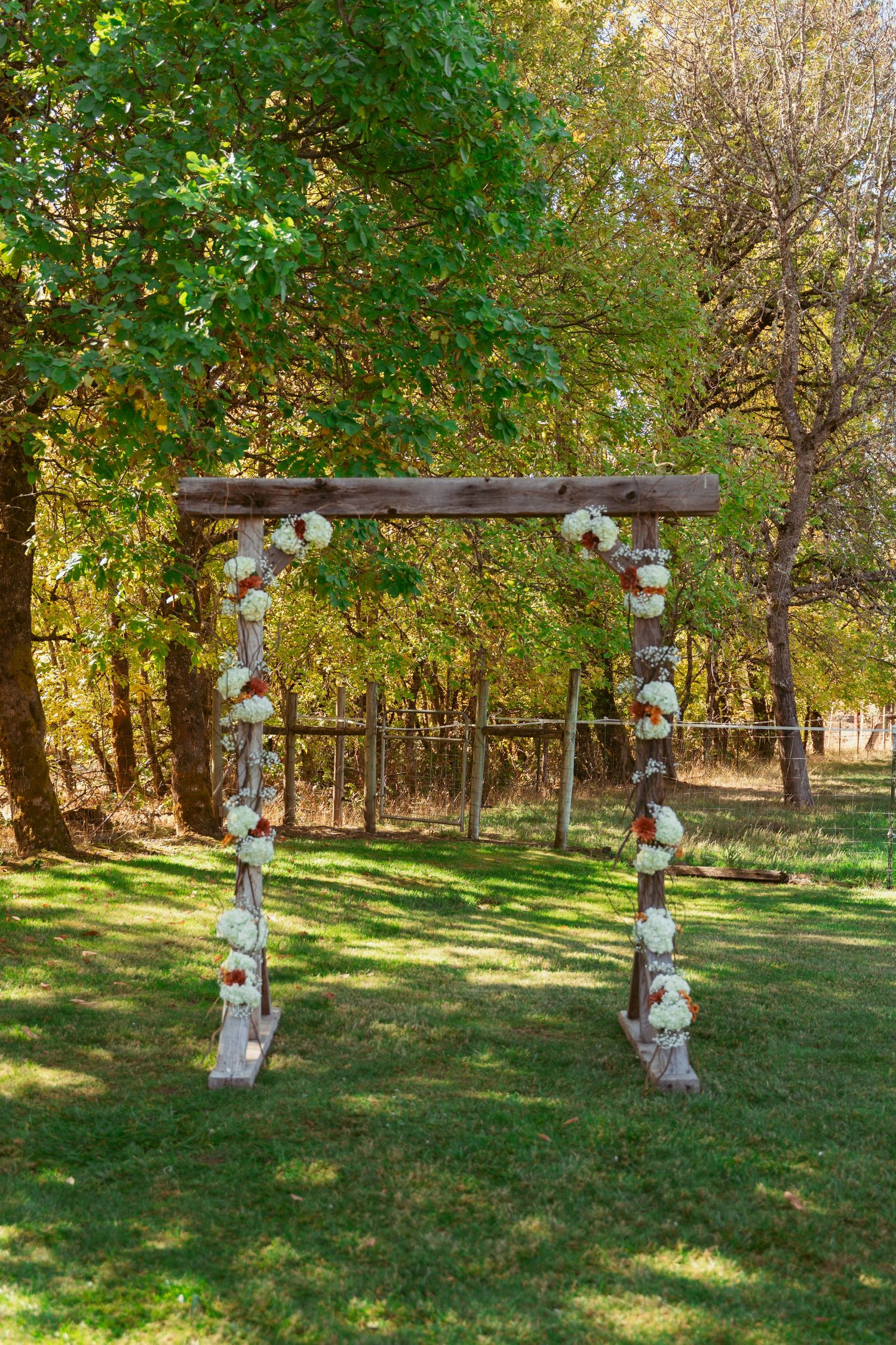 Wooden wedding arch decorated with white flowers and fabric in an outdoor garden setting.