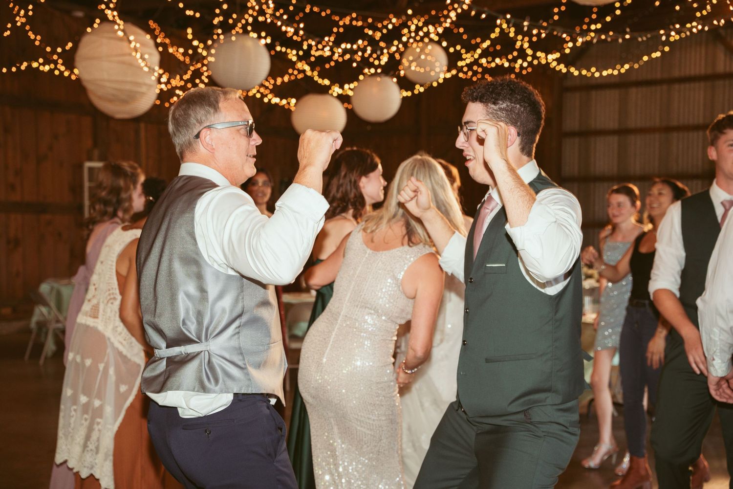 Wedding celebration in full swing under warm string lights in a rustic barn venue.