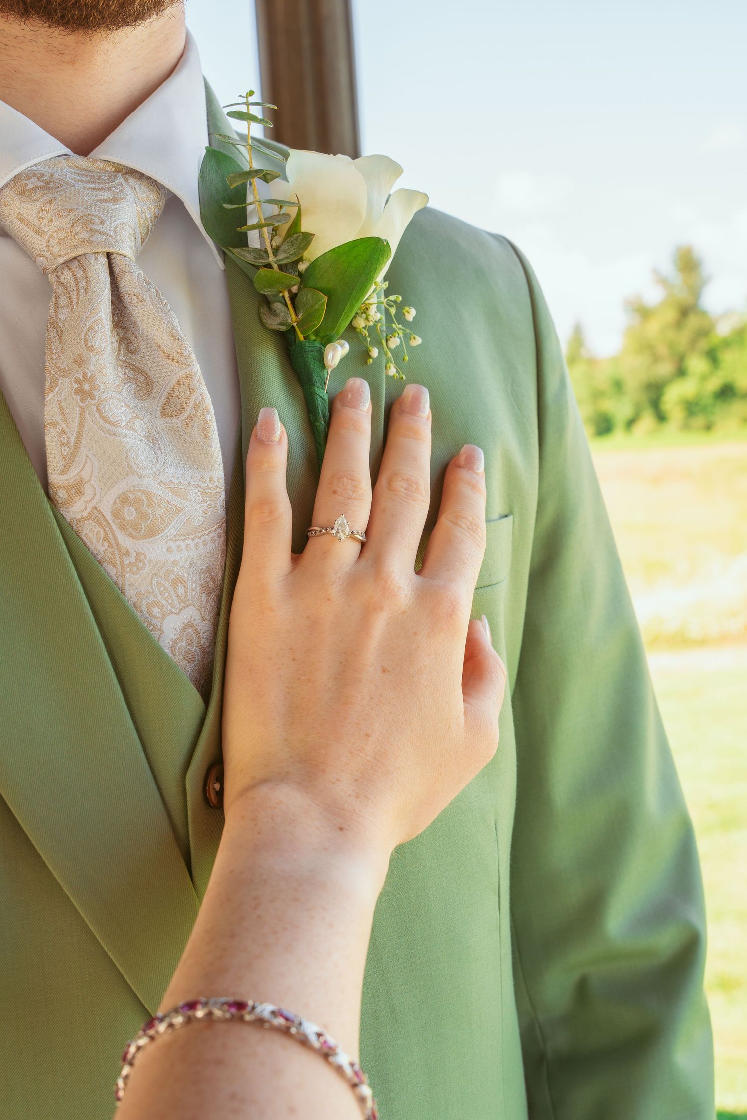 Close-up of wedding attire showing mint green suit jacket with cream paisley tie and floral boutonniere.