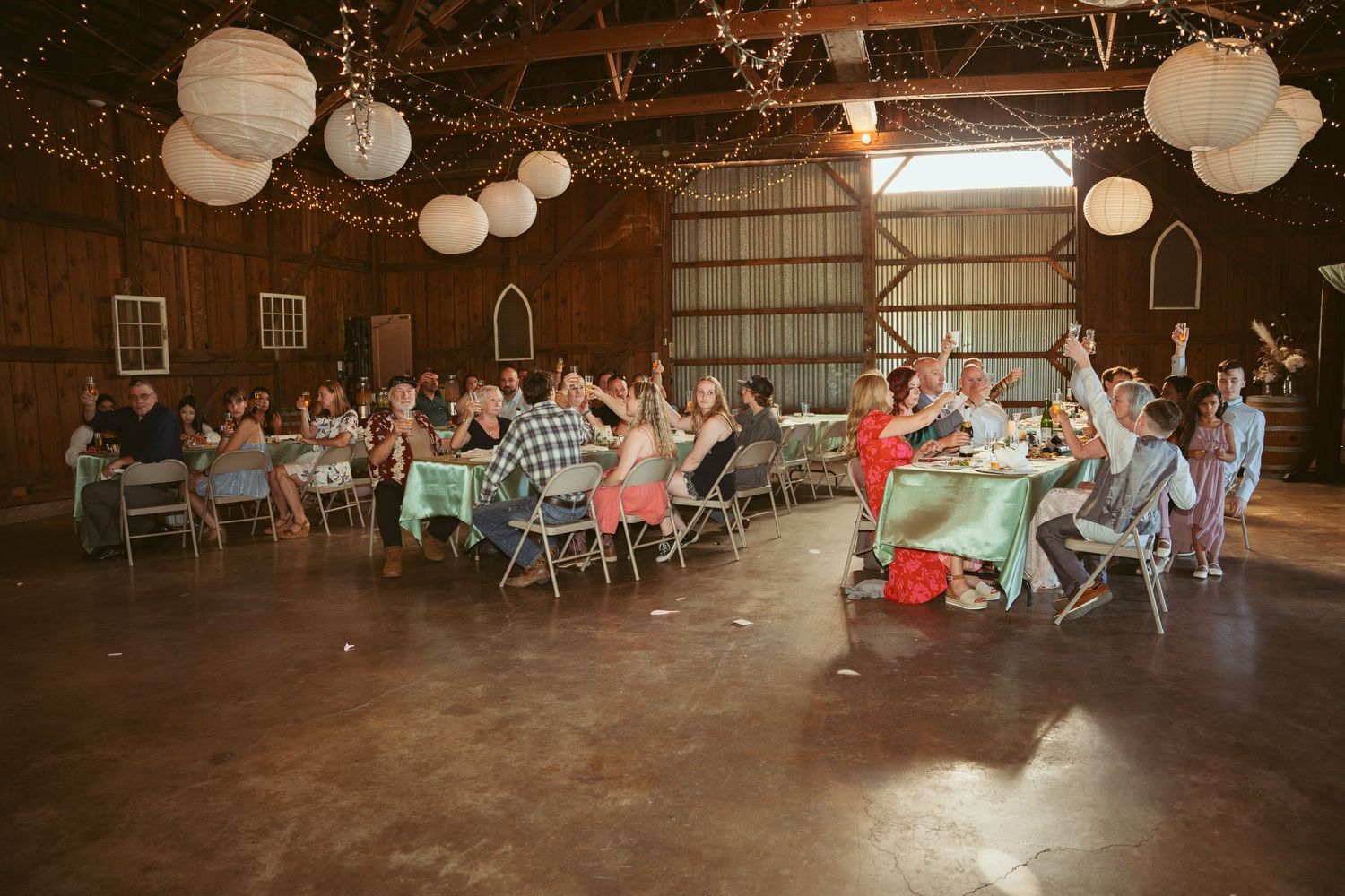 Wide view of wedding reception space with guests seated at tables in rustic barn venue.