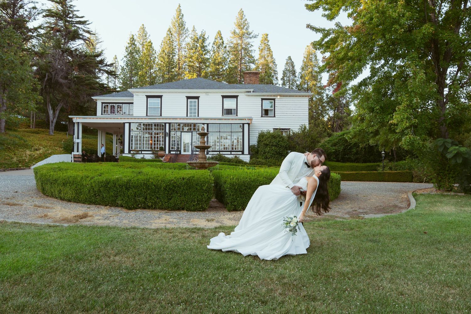 A sequence of wedding photos taken on a grassy lawn with evergreen trees and a white house in the background.