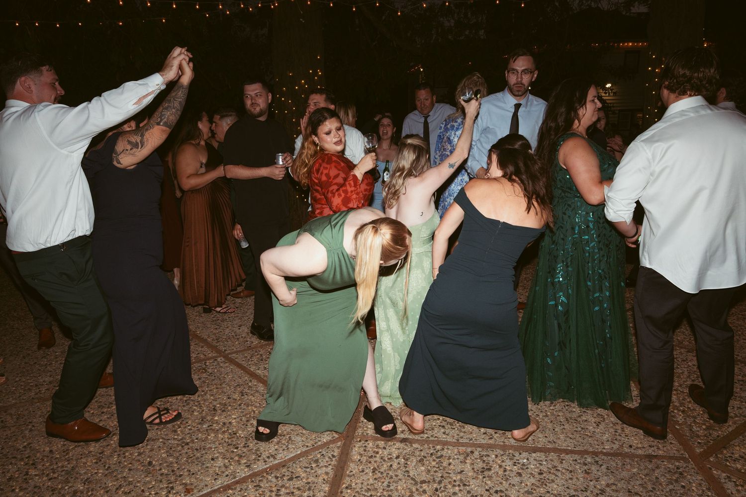 Wedding guests dancing enthusiastically on outdoor patio under string lights.