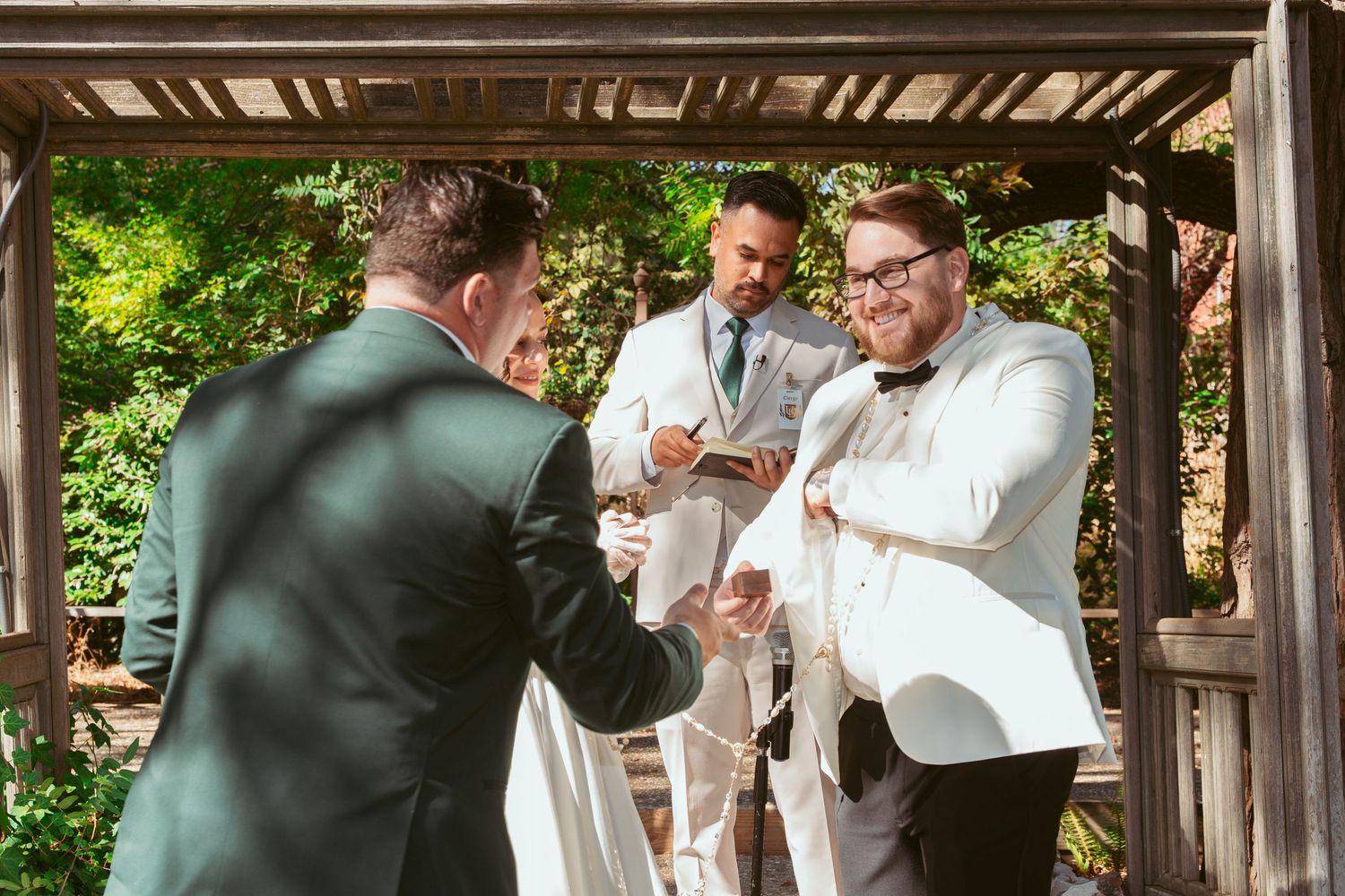 Wedding party celebrates under rustic wooden pergola during outdoor ceremony.