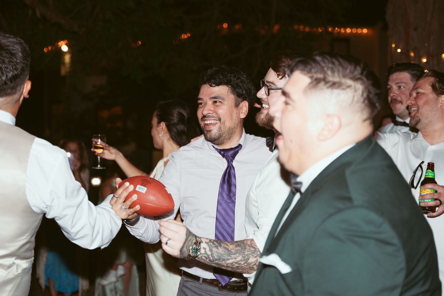 Wedding guests laughing and enjoying drinks during an evening celebration.