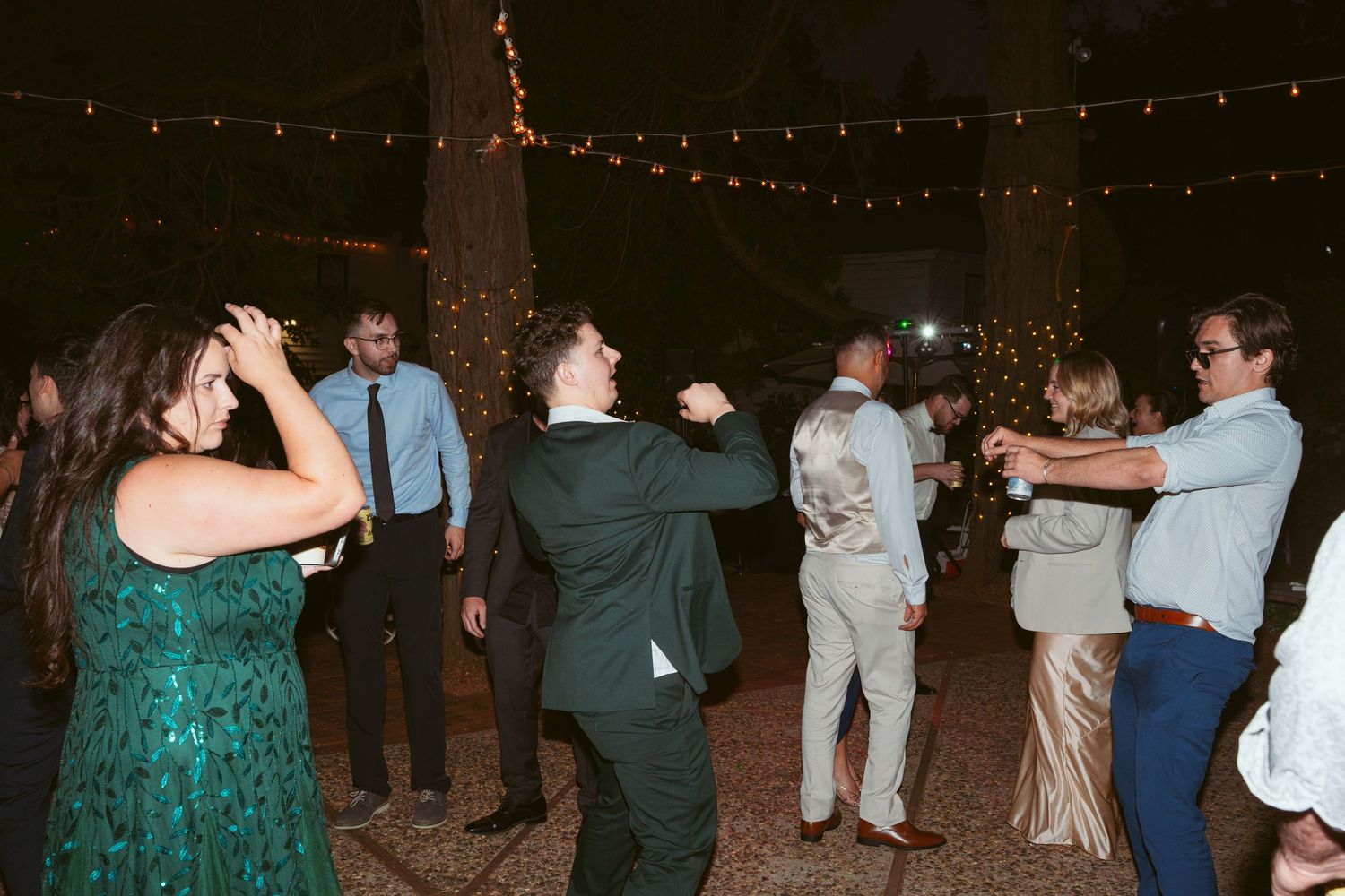 Couples dancing together at an outdoor evening reception with string lights overhead.