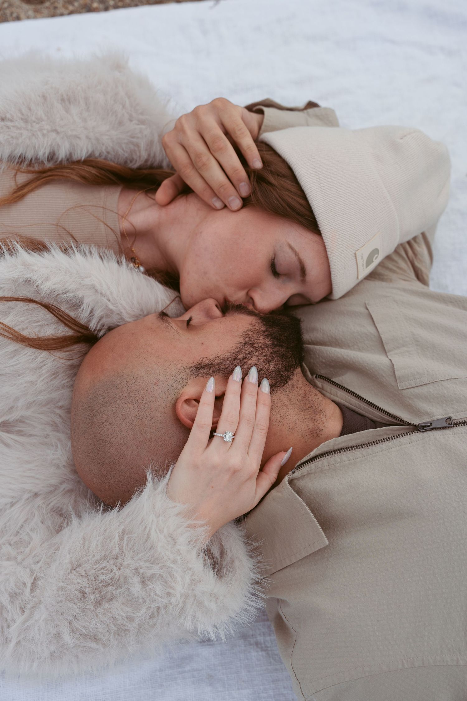 Romantic couple lying close together on white surface in soft lighting.
