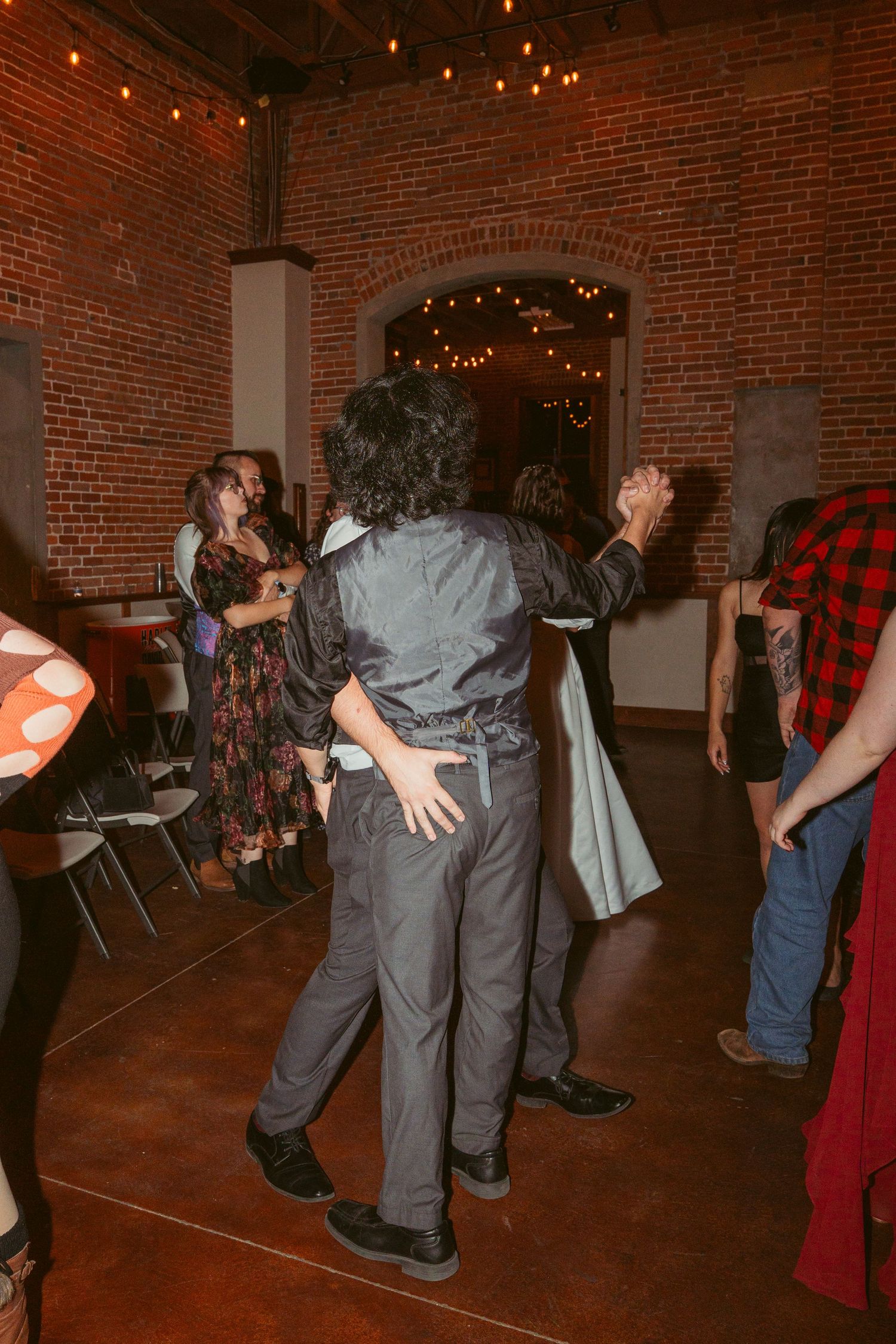 People dancing together at an indoor event space with exposed brick walls and ambient lighting.
