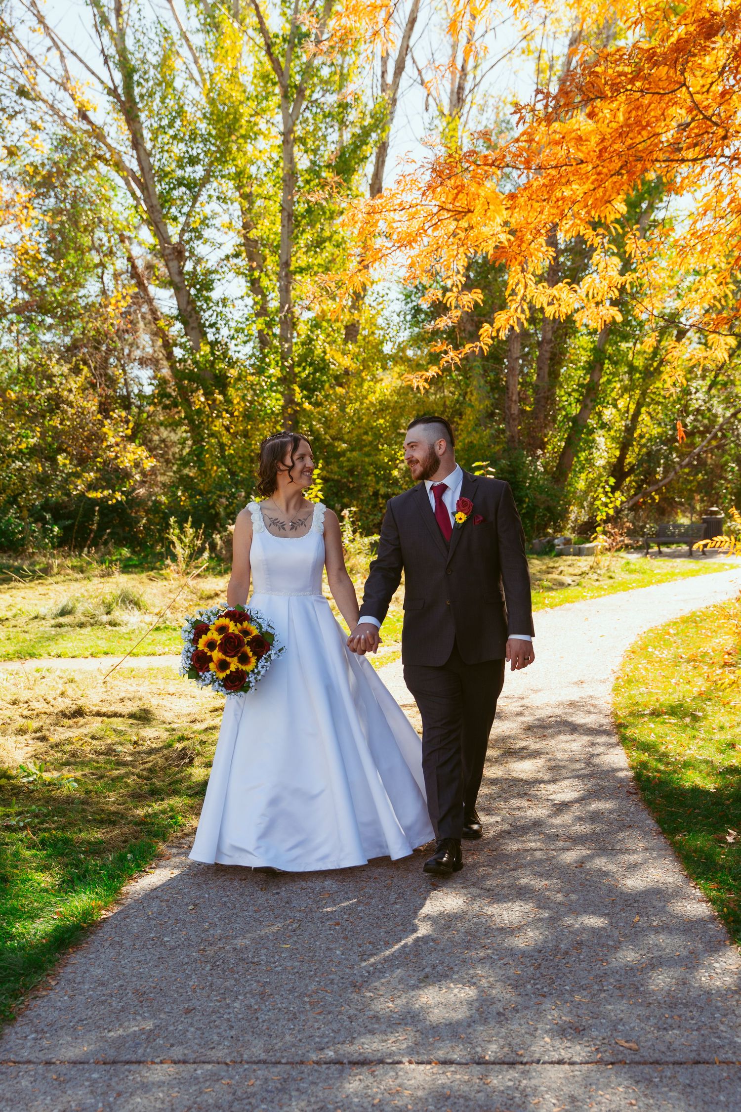 A couple strolls along a gravel path surrounded by brilliant fall foliage.